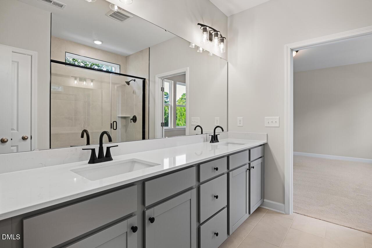 Modern dual-vanity bathroom with gray cabinets and glass-enclosed shower in The Chestnut floor plan, Aberdeen, NC.