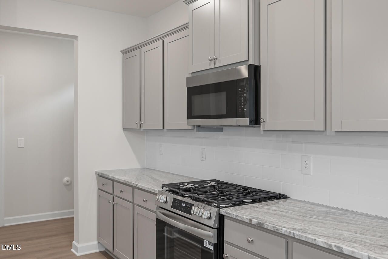 Modern kitchen featuring gray shaker cabinets, stainless steel microwave, oven, gas cooktop, and quartz countertops in Davidson Homes The Gavin B, Lillington, NC