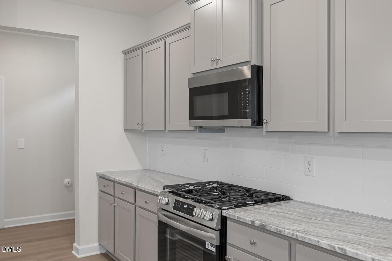Modern kitchen with gray cabinets, stainless steel gas stove, oven, and microwave on quartz countertops in Davidson Homes The Gavin B, Lillington, NC