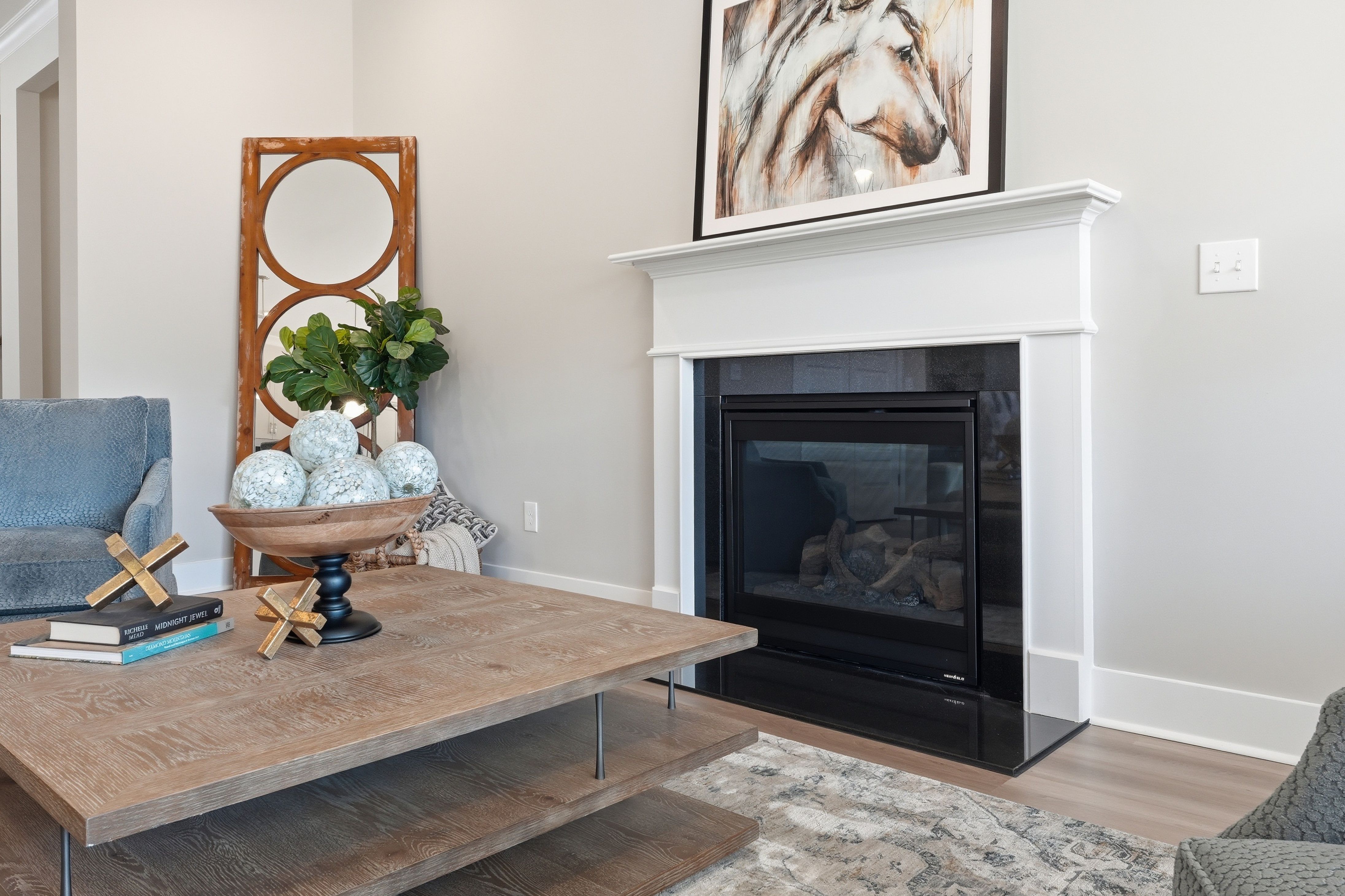 Cozy living room with white corner fireplace, wooden coffee table, and abstract horse artwork at The Meadows at Hampton Cove in Owens Cross Roads, Alabama