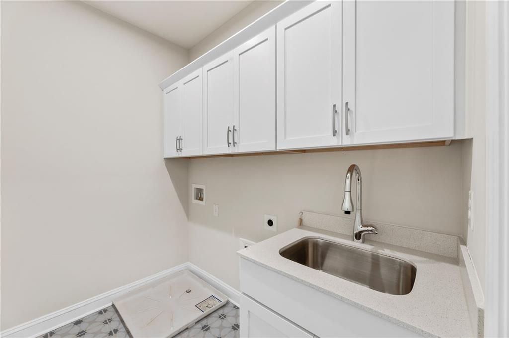 Bright laundry room with white cabinets, utility sink, and tiled floor in Davidson Homes The Danbury C, Buford, GA