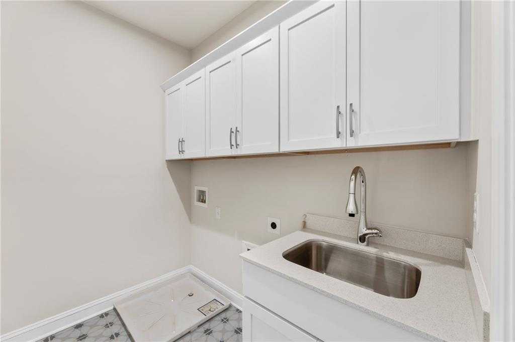 Bright laundry room with white cabinets, utility sink, and tiled floor in Davidson Homes The Danbury C, Buford, GA