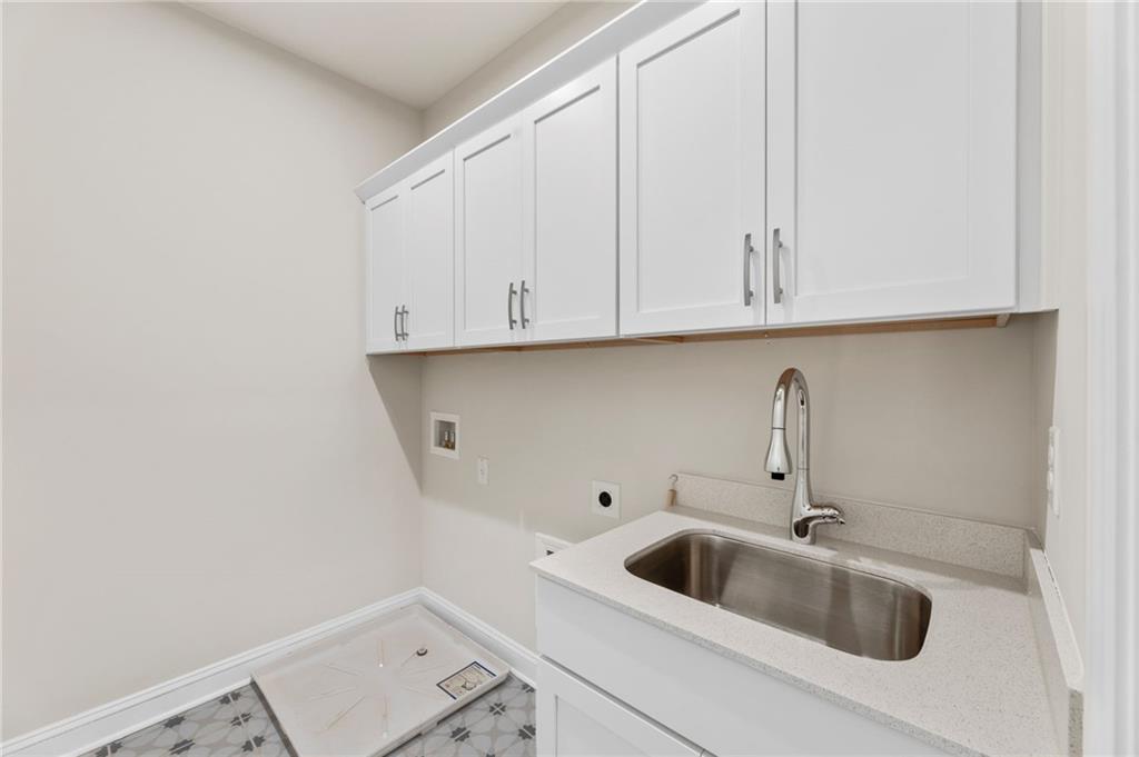 Bright laundry room with white cabinets, utility sink, and tiled floor in Davidson Homes The Danbury C, Buford, GA