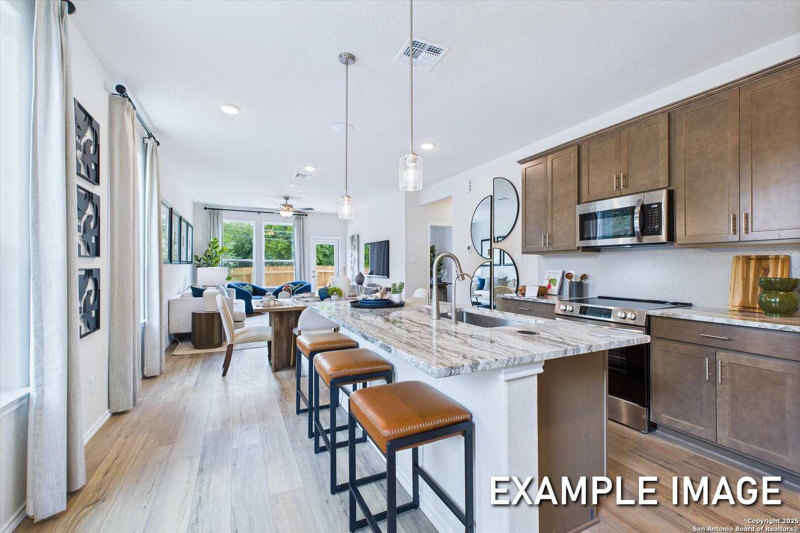 Open-concept kitchen with white granite island, brown cabinets, and stainless appliances in The Gillian B, San Antonio, TX