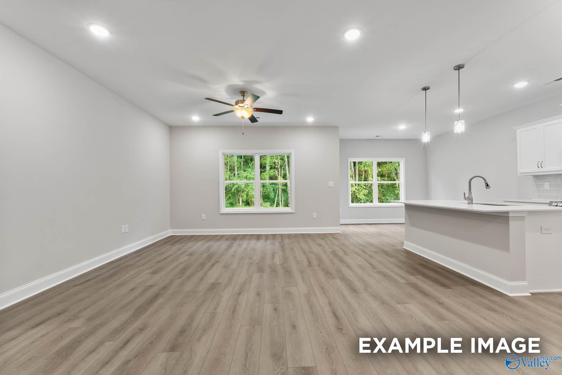 Open-concept living kitchen with light wood floors, gray walls, large windows, ceiling fan, and white island in The Asheville 3-bedroom home, Huntsville AL