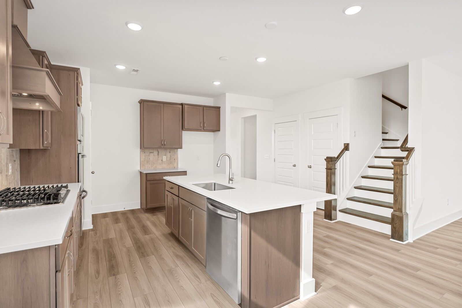 Open-concept kitchen with wood cabinets, white quartz island, stainless appliances, and adjacent staircase in Davidson Homes The Ash C, Mt. Juliet, TN