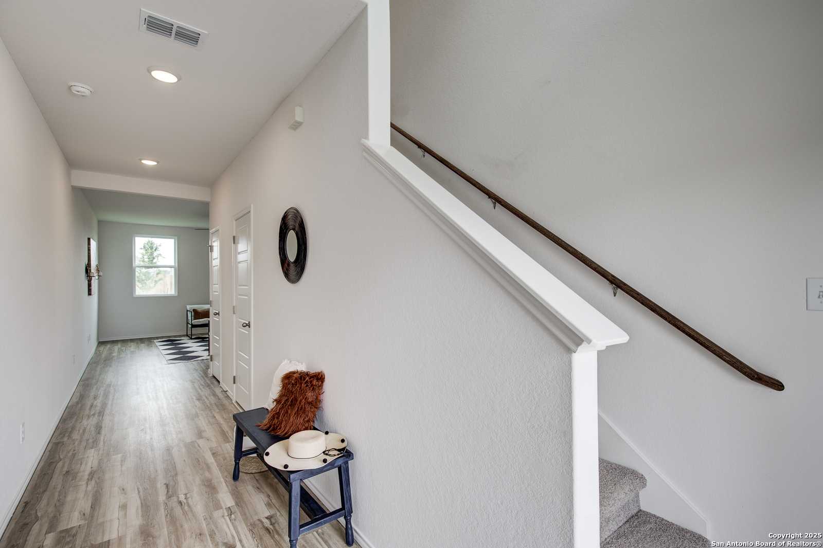 Bright hallway with luxury vinyl plank floors, wooden staircase, and decorative bench in The Trinity A 4-bedroom home, San Antonio