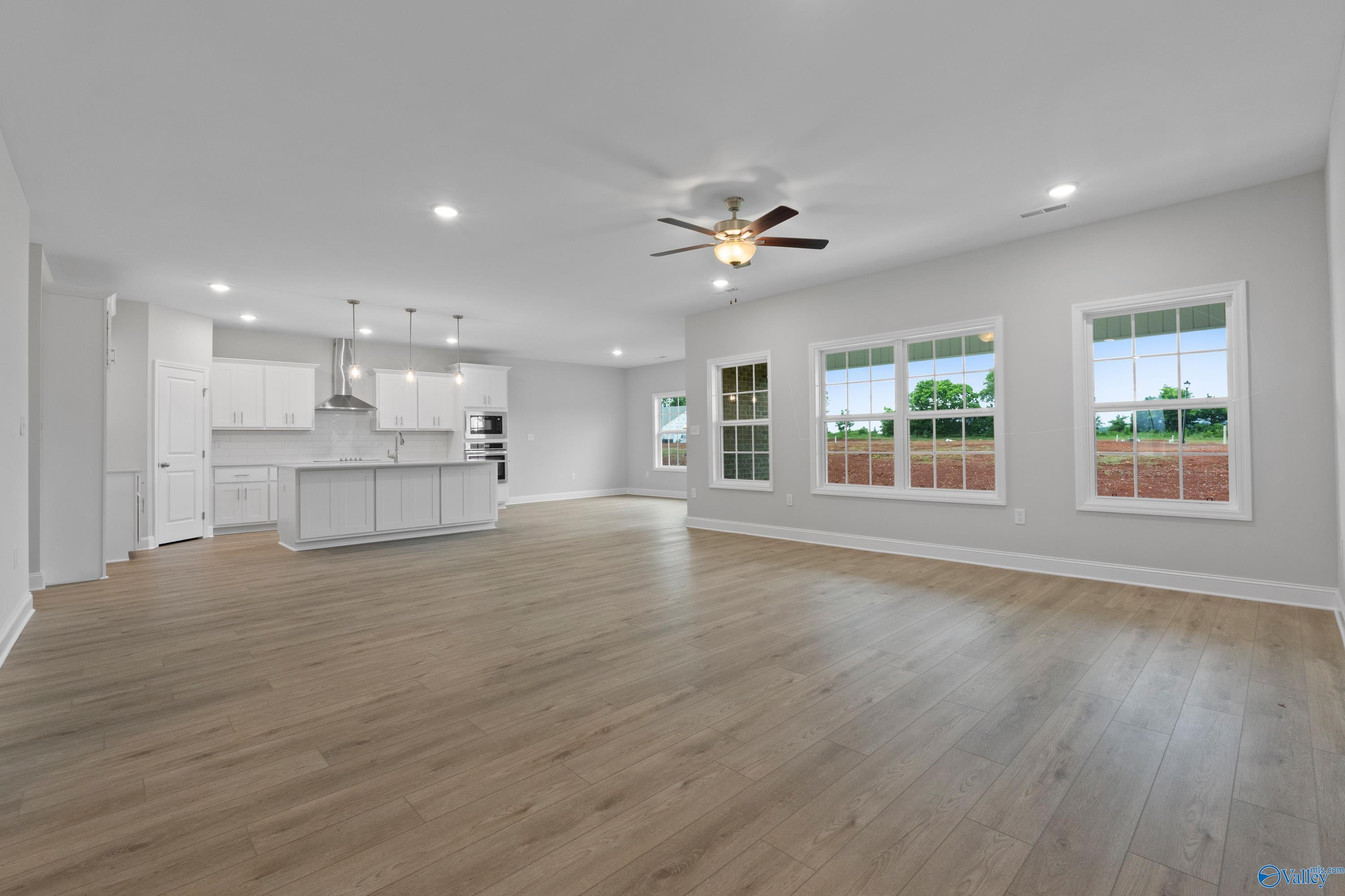 Spacious open-concept great room with white island kitchen, large windows, ceiling fan in Davidson Homes Rockford B, Toney, AL