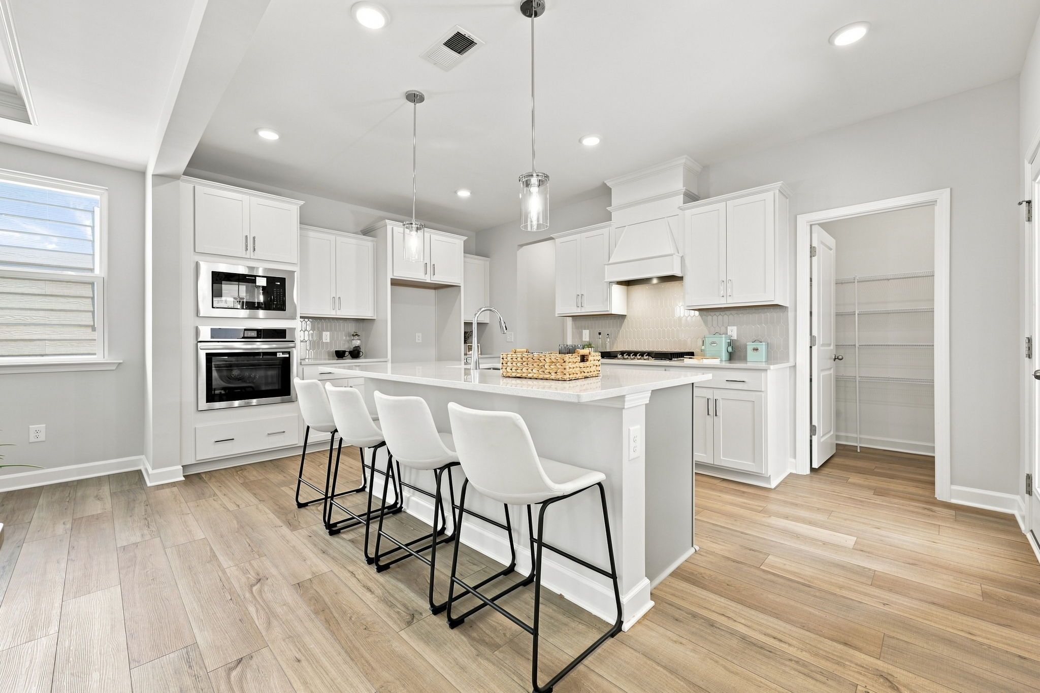 Modern kitchen in The Jordan A featuring white cabinets, a spacious center island with seating, and a walk-in pantry.