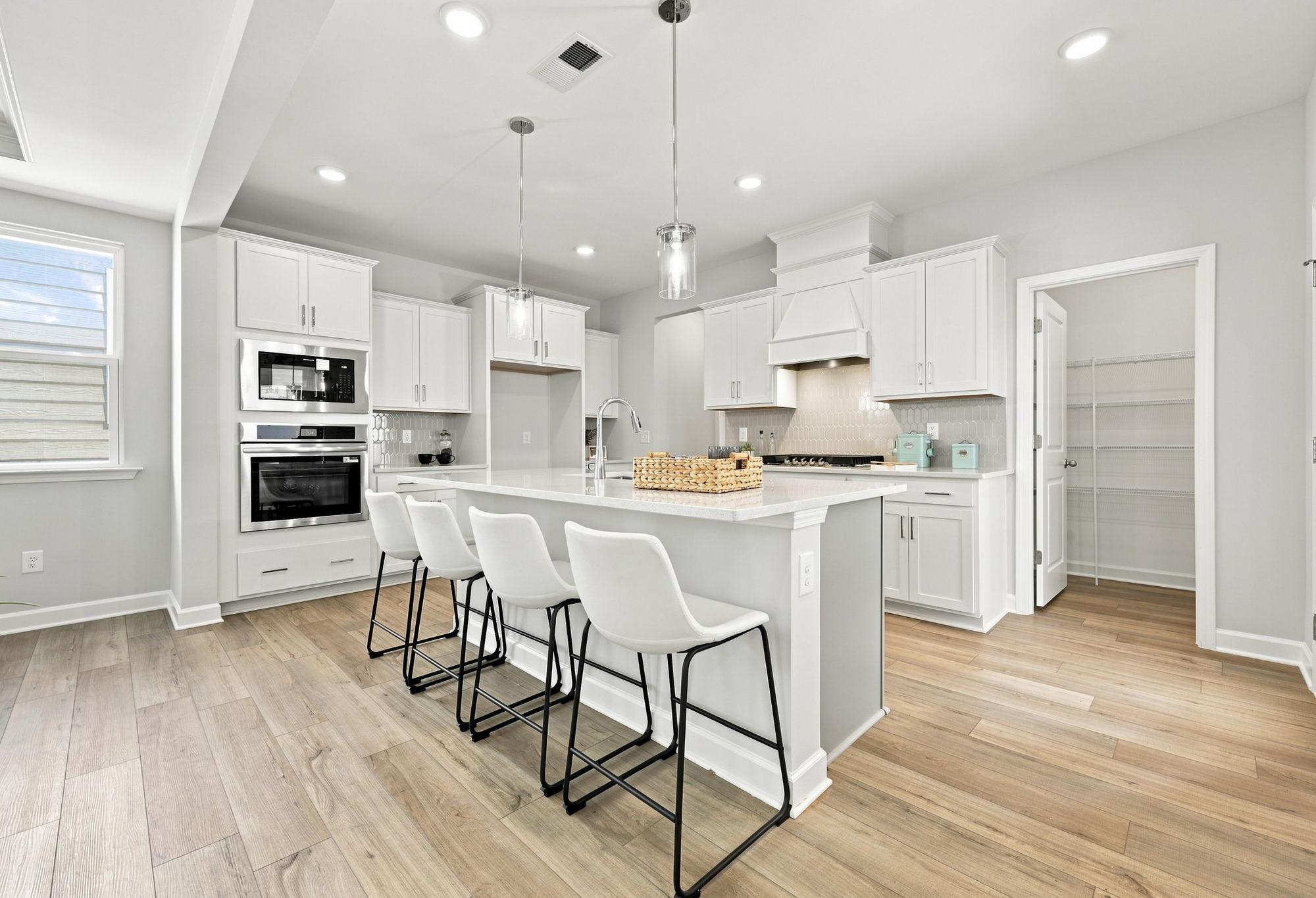 Modern kitchen in The Jordan A featuring white cabinets, a spacious center island with seating, and a walk-in pantry.