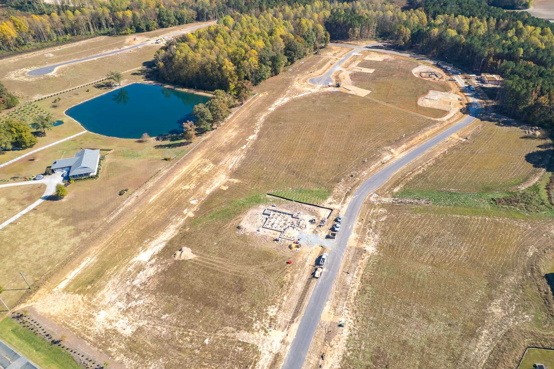 Aerial view of Prince Place development in Fuquay-Varina NC with pond, dirt roads, construction sites, and autumn woods