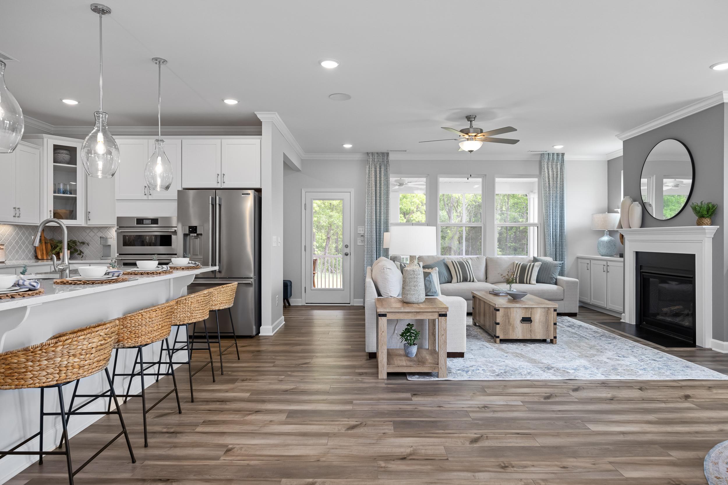 Open-concept kitchen and living room at Tobacco Road in Angier NC with white cabinets, island bar stools, hardwood floors, and gray sofa by fireplace