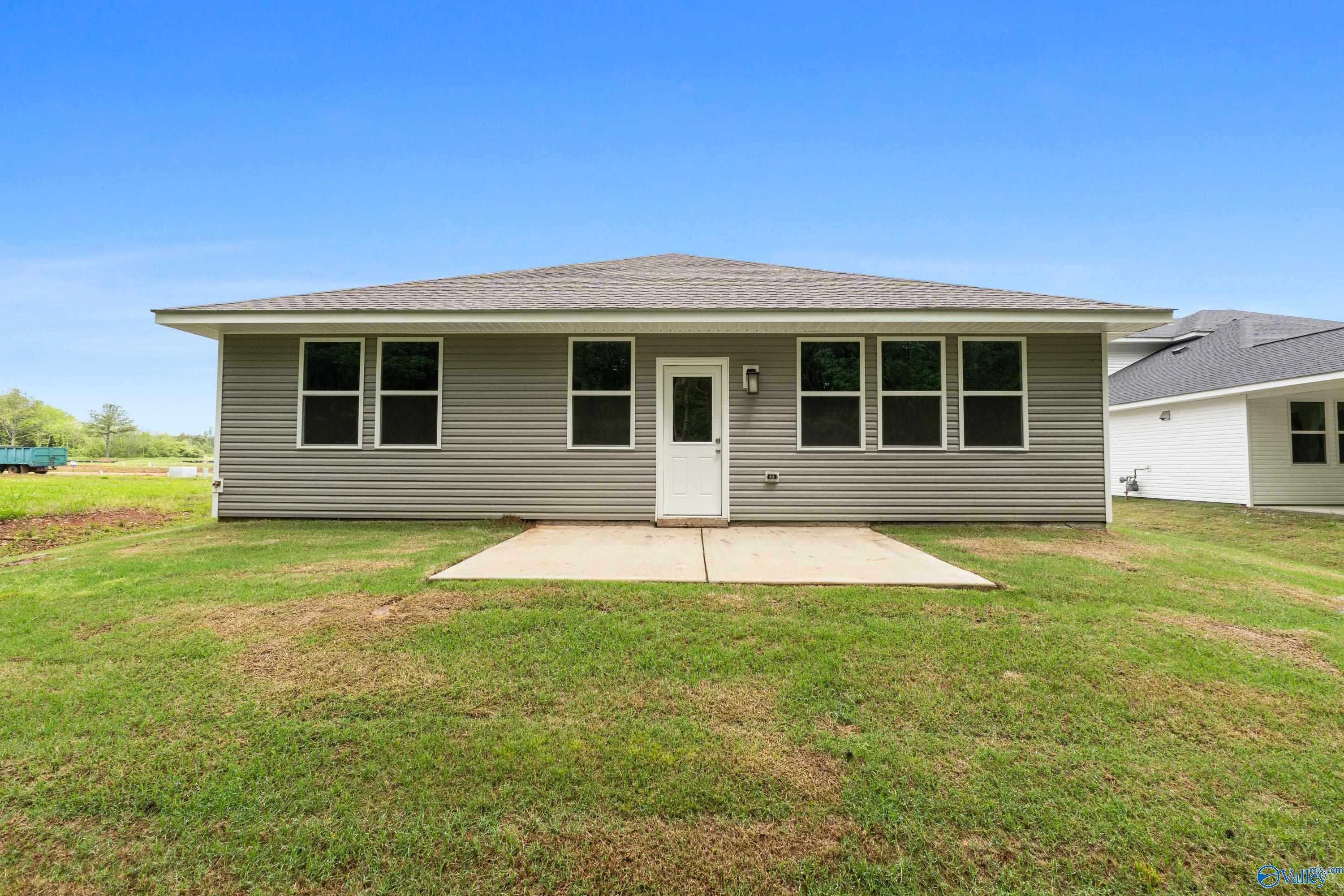 Rear view of Davidson Homes The Luna: single-story gray siding house with concrete patio, windows, and green yard in Forest Glen, Hazel Green