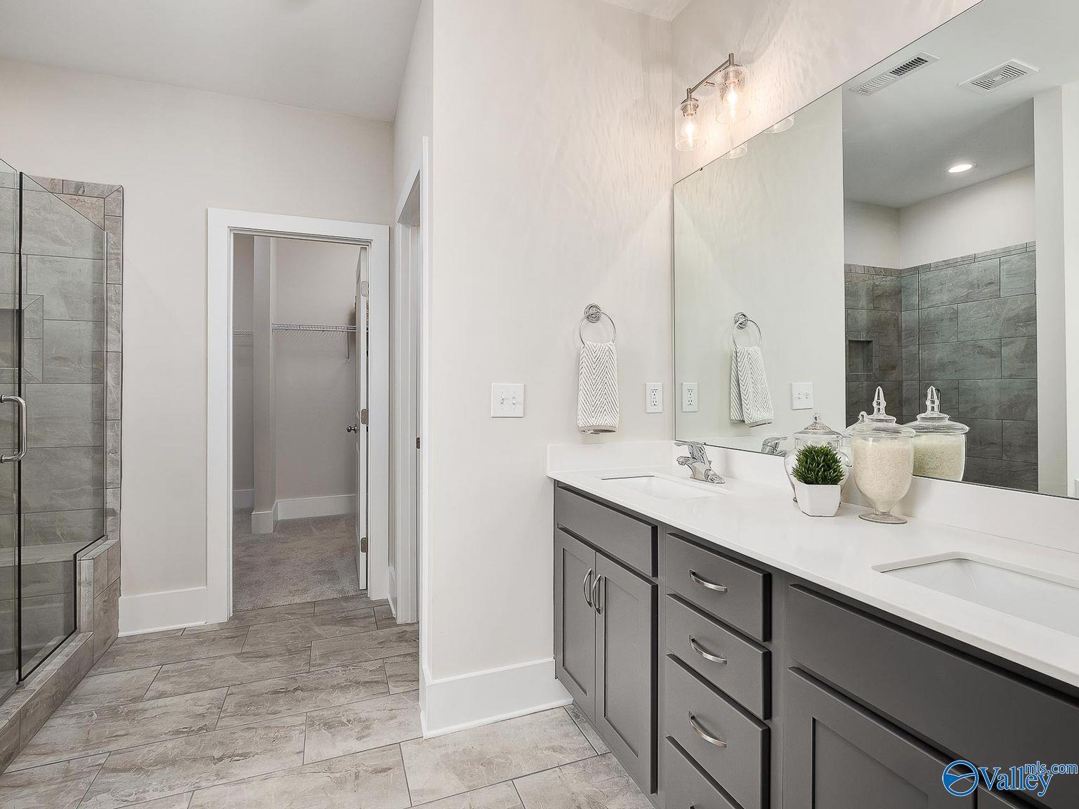 Modern master bathroom featuring double vanity, frameless glass shower, and adjacent walk-in closet in Davidson Homes The Everett, Toney, Alabama