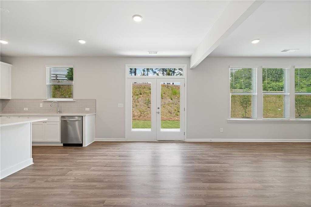 Bright open kitchen with white cabinets, island, stainless dishwasher, and French doors to wooded backyard in Davidson Homes The Hickory B, Winder GA