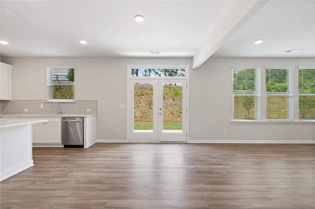 Open kitchen-living space with white island, stainless sink, hardwood floors, and French doors to green backyard in Davidson Homes The Hickory A, Winder GA