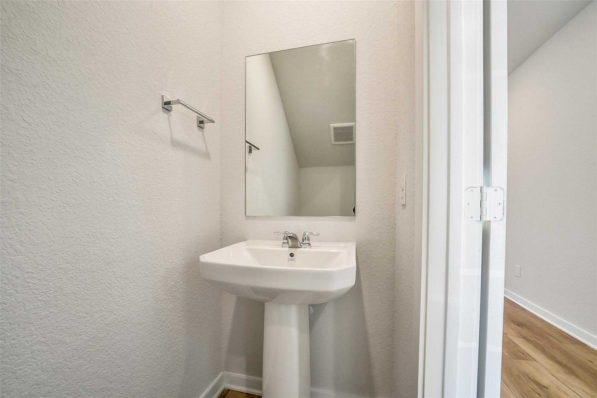 Compact powder room with white pedestal sink, chrome faucet, and framed mirror in Davidson Homes Trinity F, Magnolia, Texas