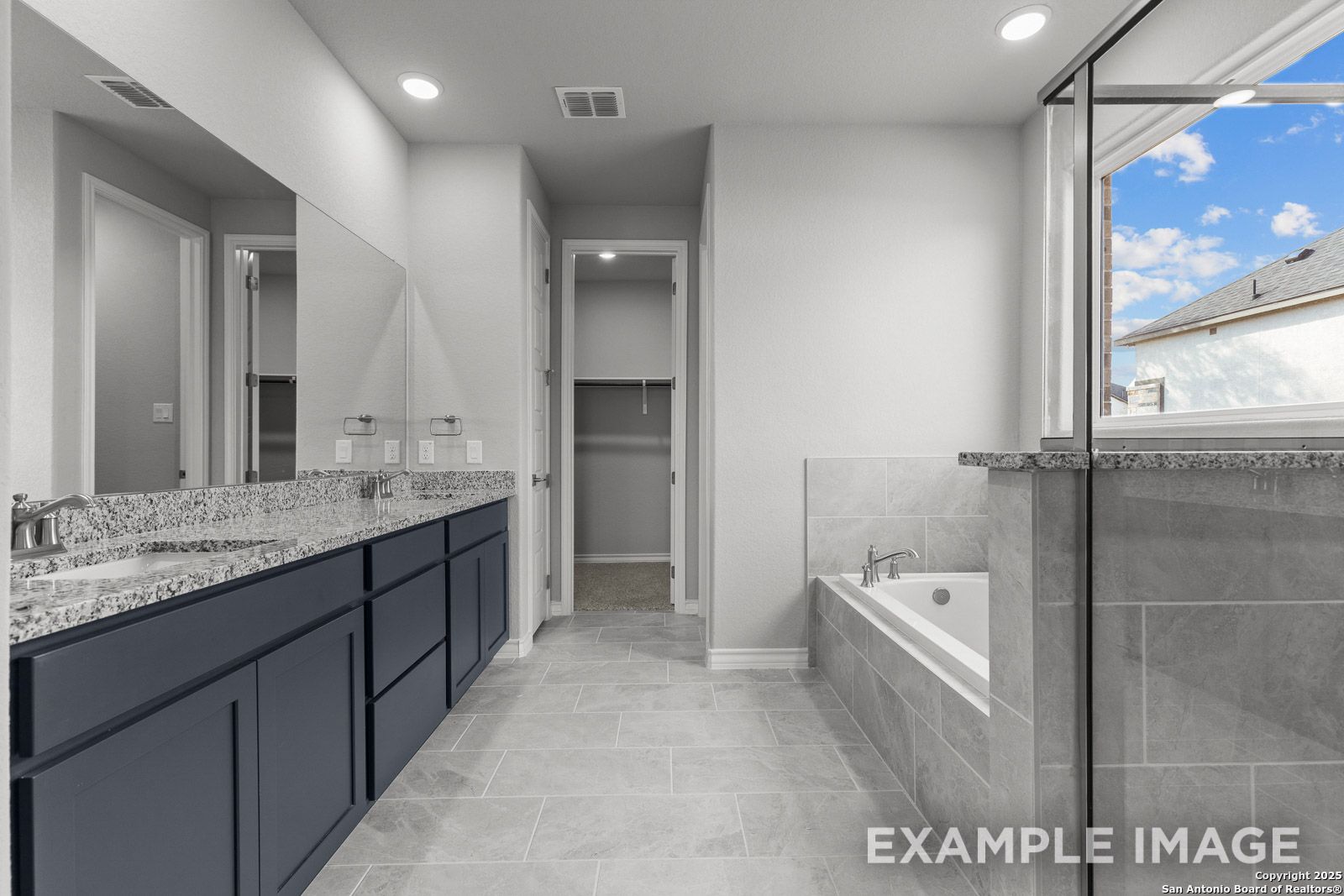 Luxurious master bathroom in The Oxford featuring a dual-sink vanity, soaking tub, and walk-in closet in Castroville, TX.