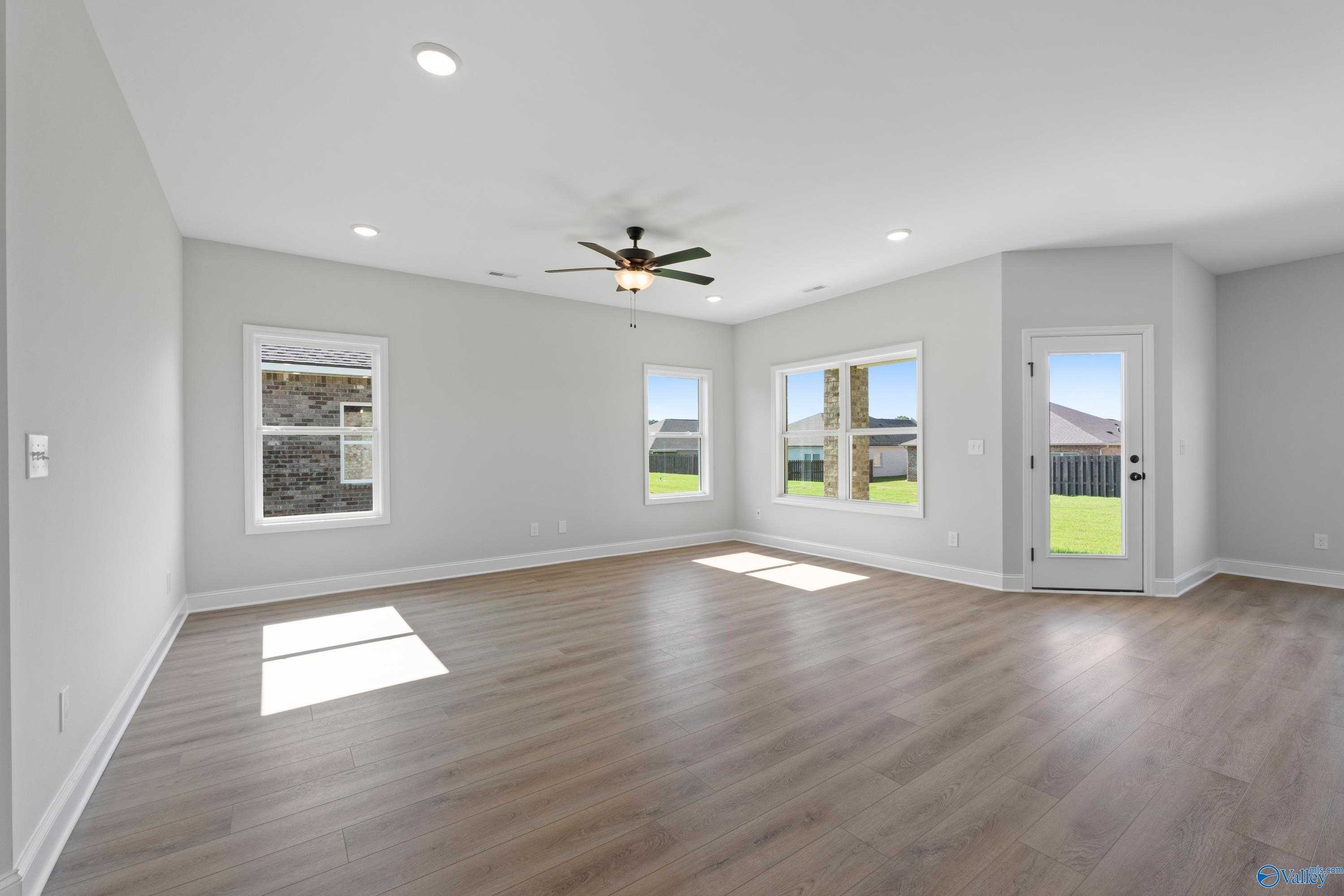 Bright living room with light gray walls, hardwood floors, large sunny windows, and ceiling fan in Davidson Homes The Franklin C, Hazel Green, AL