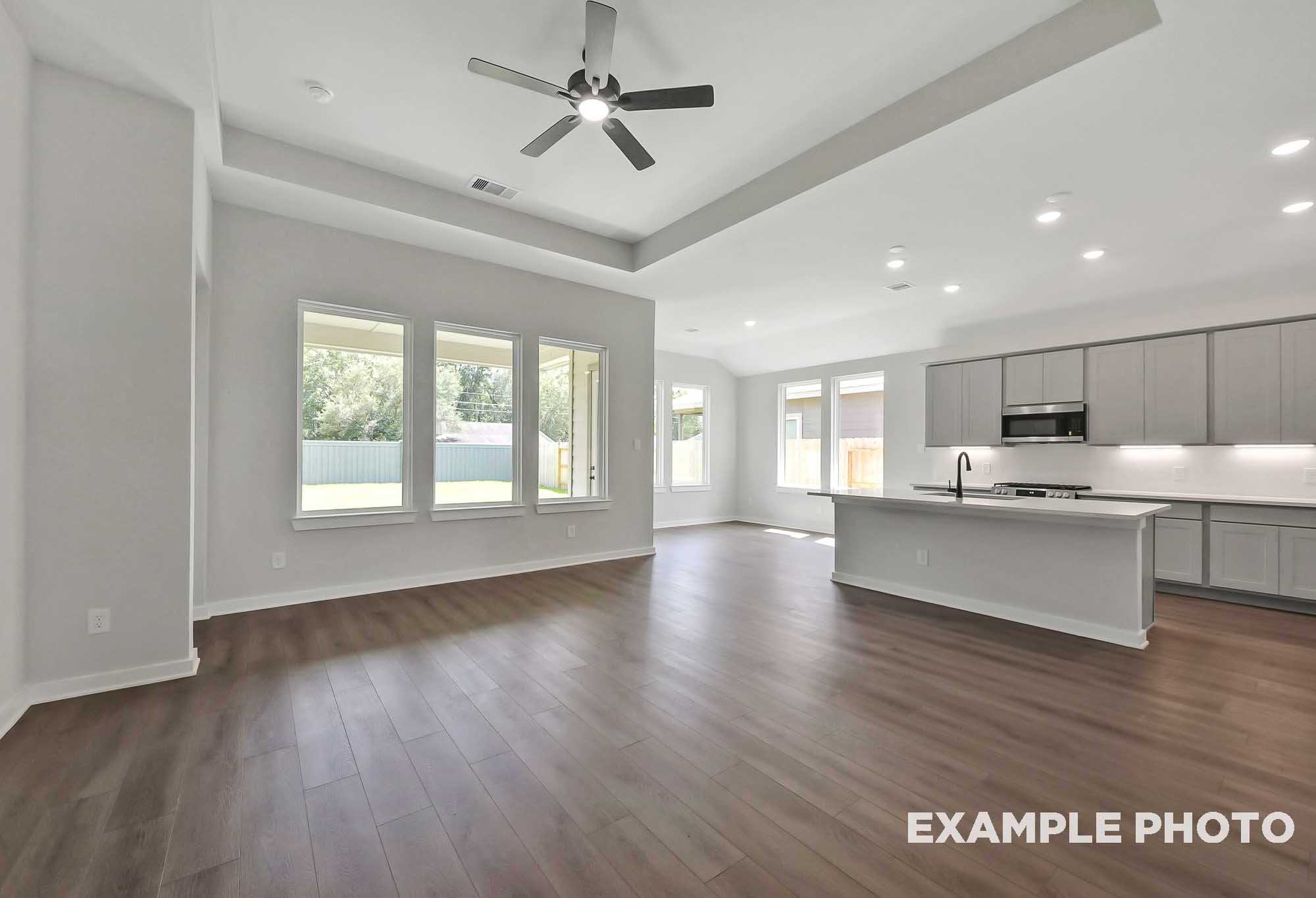 Spacious open-concept kitchen and living area in The Sequoia home by Davidson Homes featuring white cabinets, large island, ceiling fan, and large windows