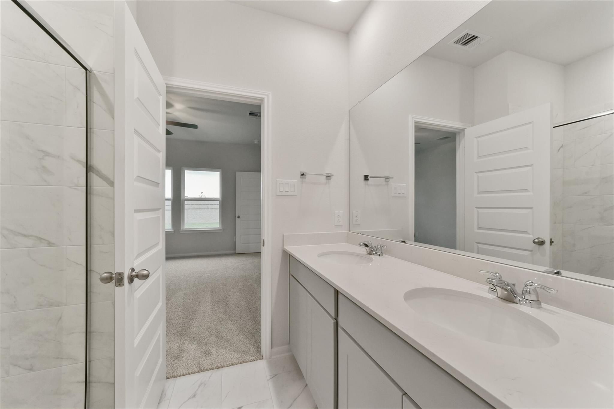 Modern master bathroom featuring double vanity with white cabinets and mirrors in Davidson Homes San Marcos E, Beasley, Texas