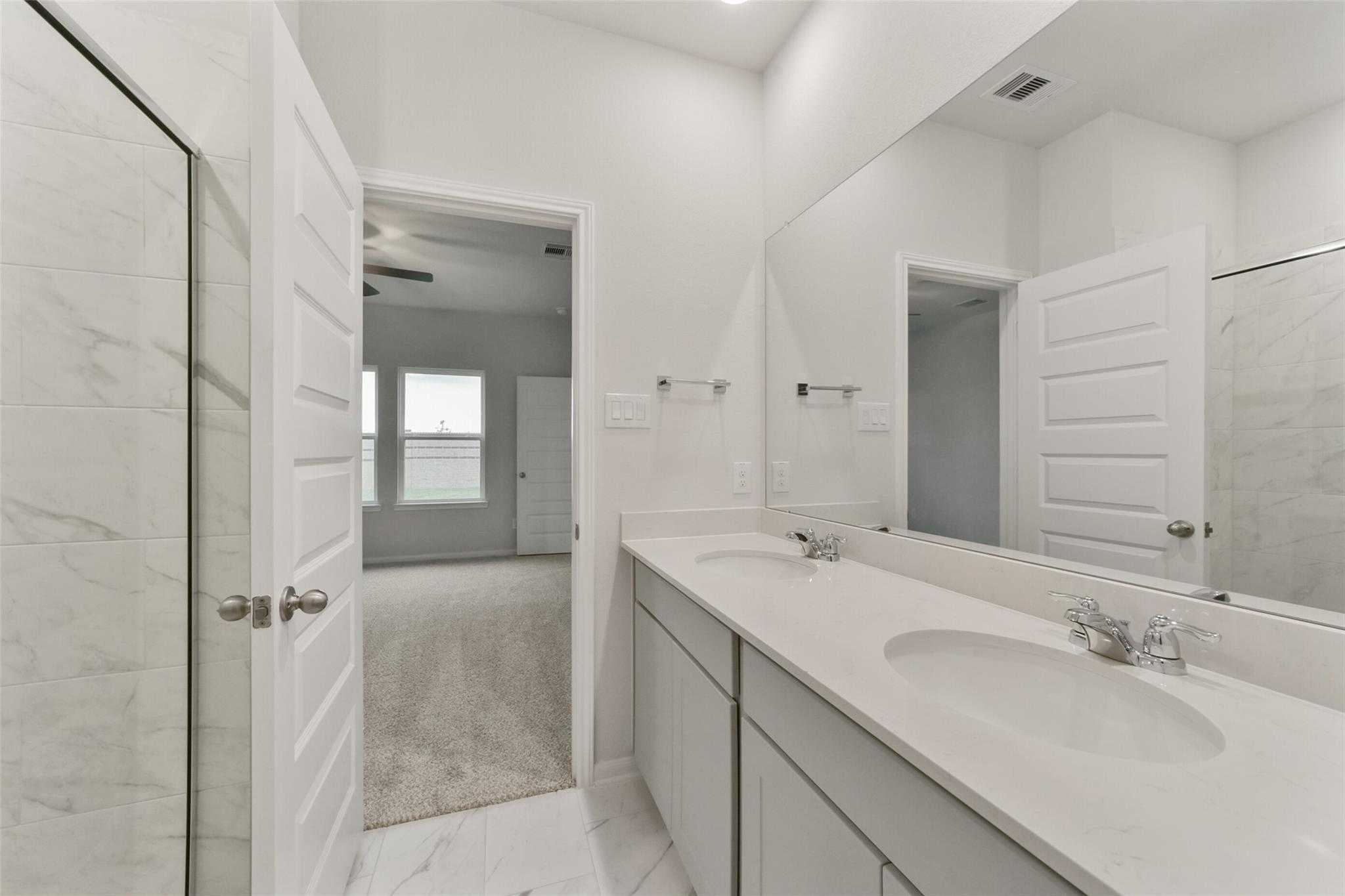 Modern master bathroom featuring double vanity with white cabinets and mirrors in Davidson Homes San Marcos E, Beasley, Texas