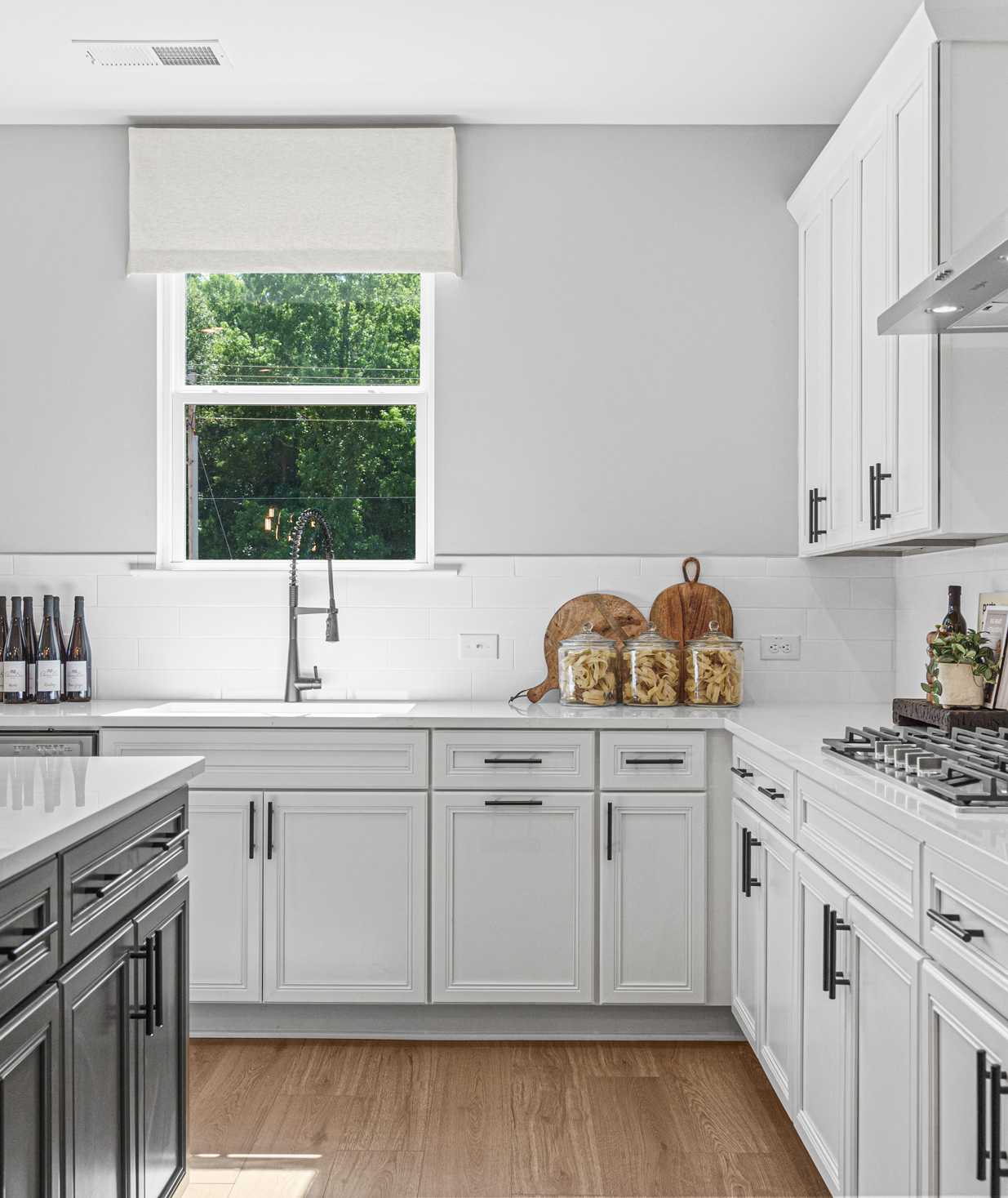 Spacious modern kitchen in Cedar Farms Winder GA with white shaker cabinets, dark quartz island, gas cooktop, and hardwood floors