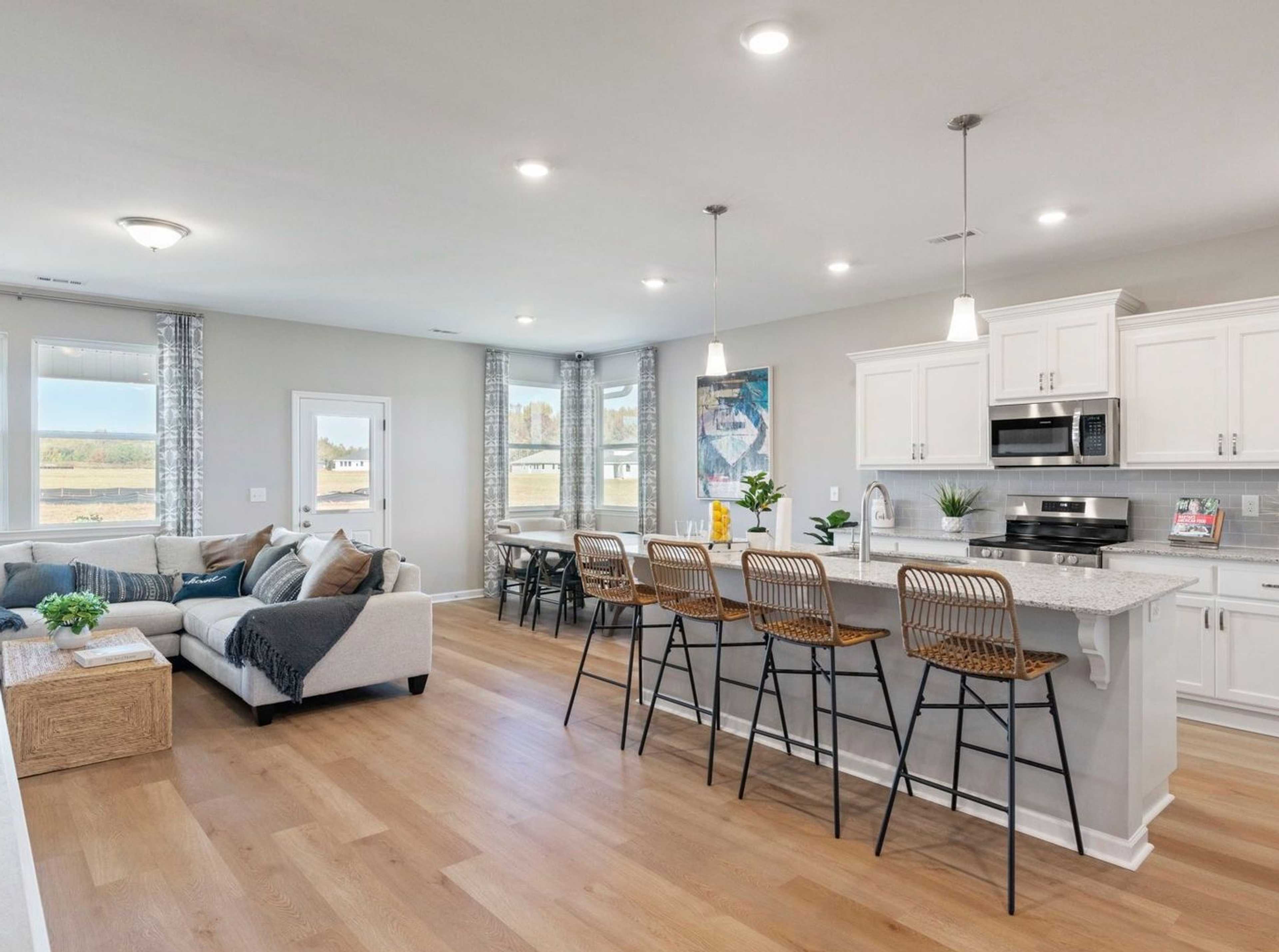 Open-concept kitchen and living room at Anderson Lakes in Opelika Alabama with hardwood floors white cabinets island bar and large windows