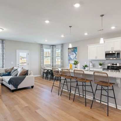 Open-concept kitchen and living room at Anderson Lakes in Opelika Alabama with hardwood floors white cabinets island bar and large windows