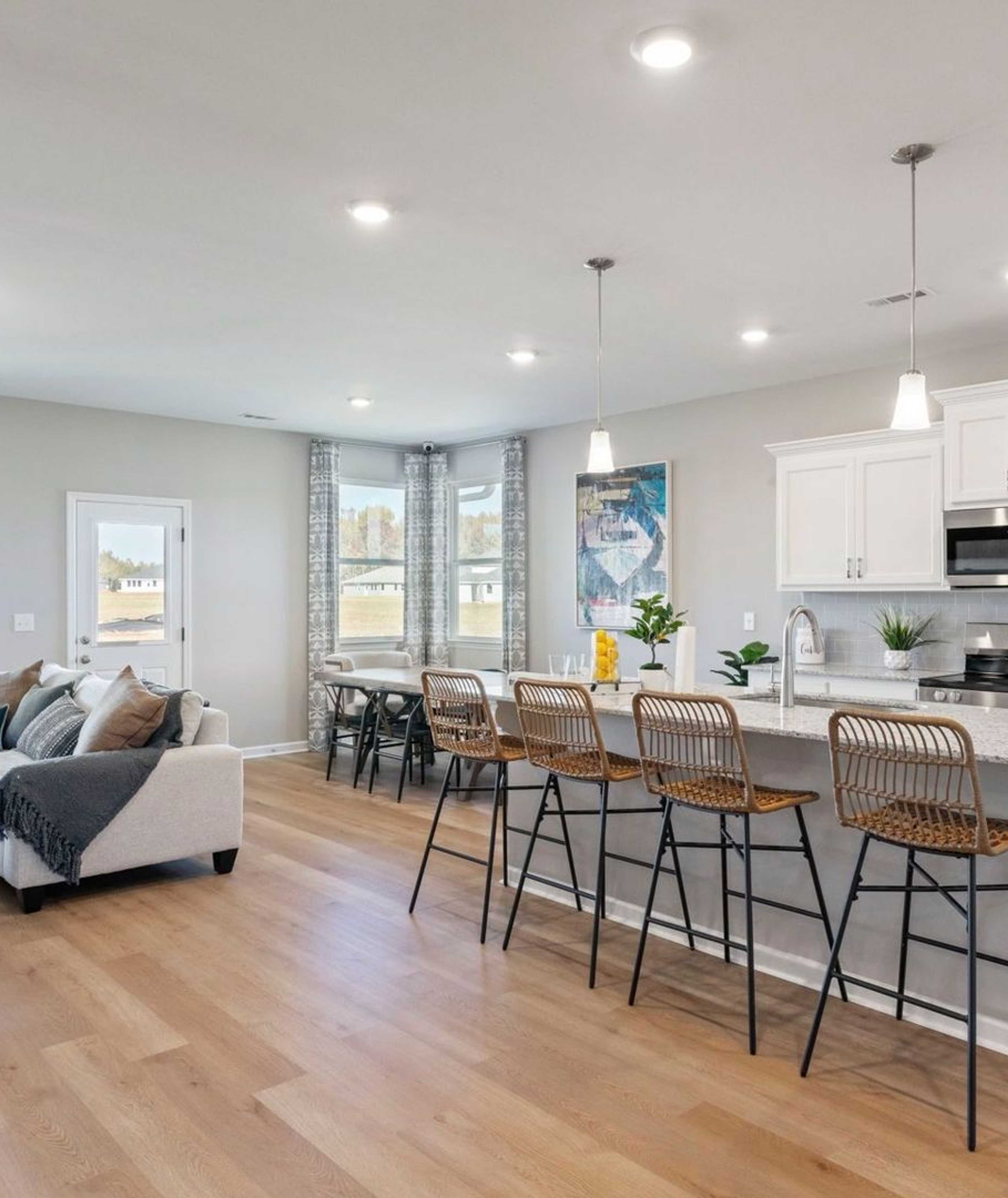 Open-concept kitchen and living room at Anderson Lakes in Opelika Alabama with hardwood floors white cabinets island bar and large windows
