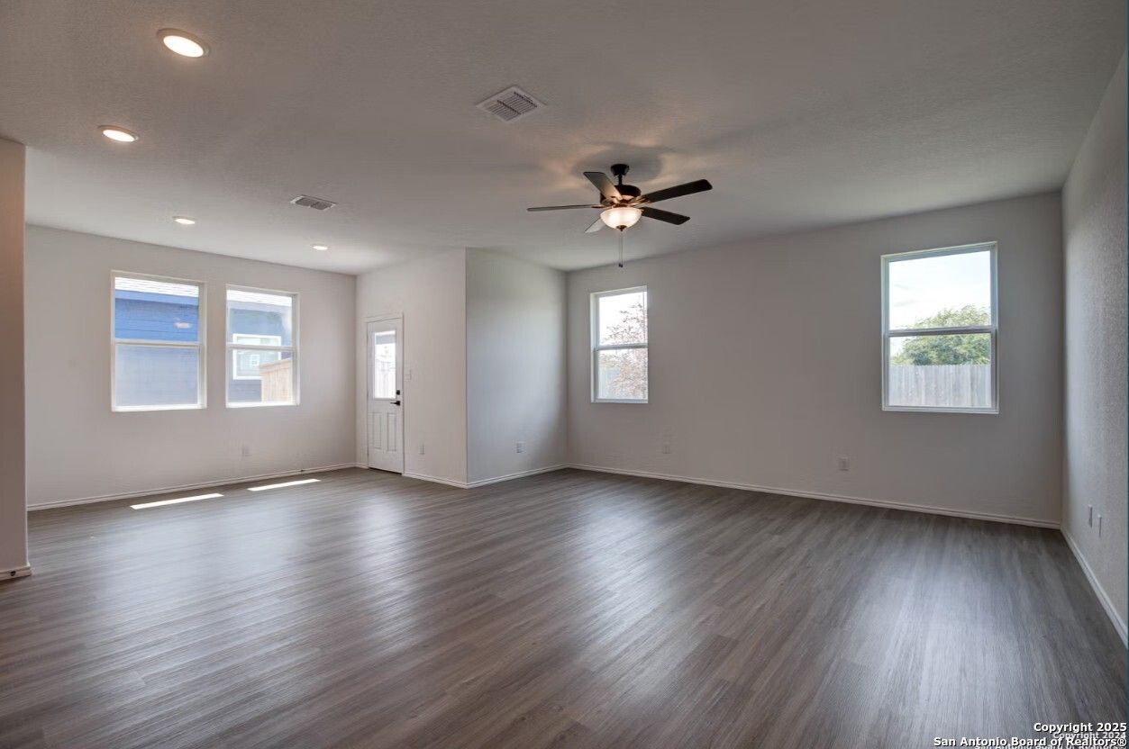 Bright open living room with gray laminate floors, ceiling fan, large windows, and recessed lighting in The Daphne H home, Seguin Texas