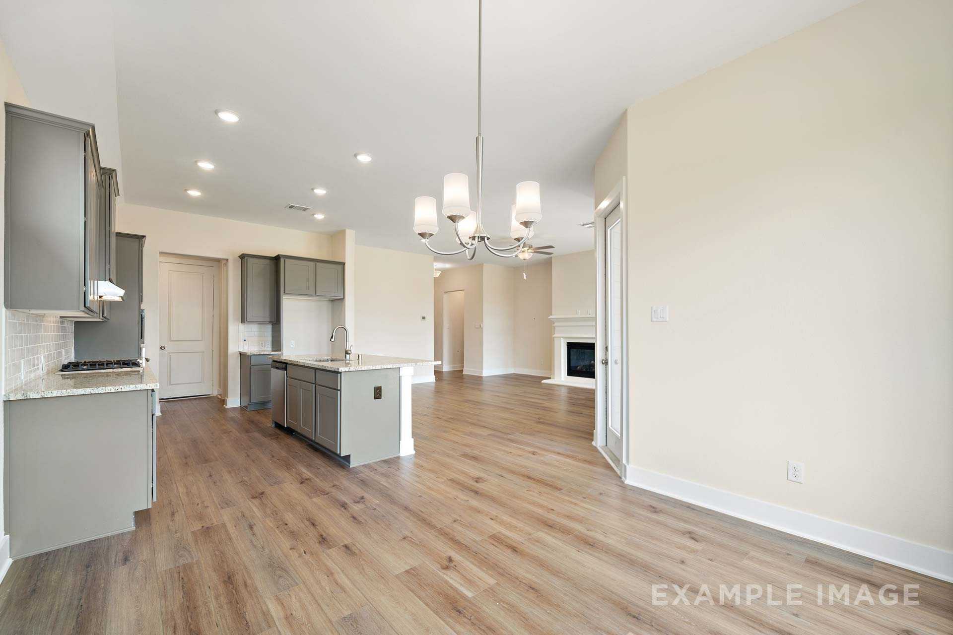 Spacious open-concept kitchen in The Diana C with gray cabinets, large island, hardwood floors, and adjacent living area with fireplace