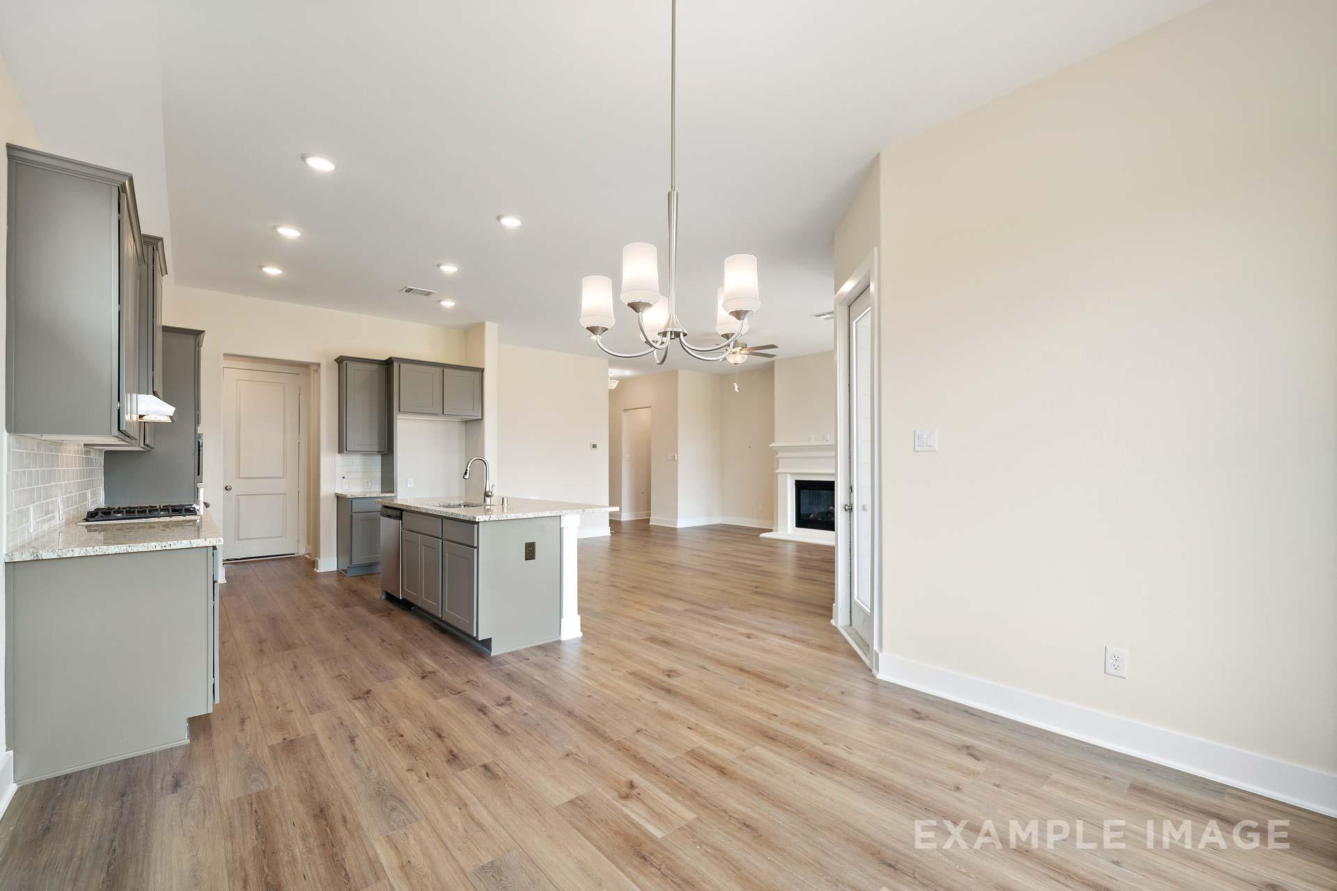 Spacious open-concept kitchen in The Diana C with gray cabinets, large island, hardwood floors, and adjacent living area with fireplace