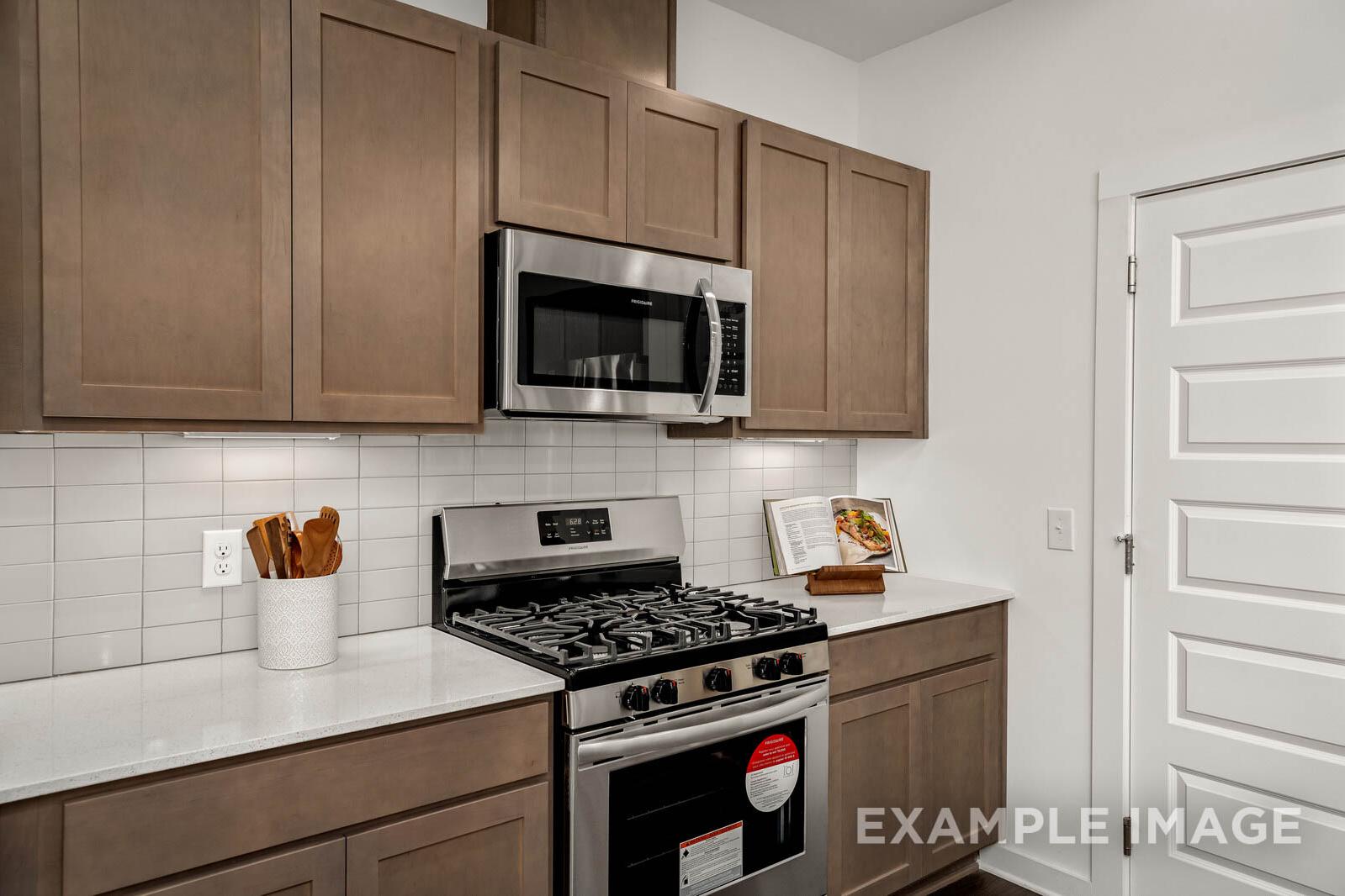 Spacious kitchen in The Gordon C featuring taupe shaker cabinets, stainless steel gas range, microwave, white subway tile backsplash