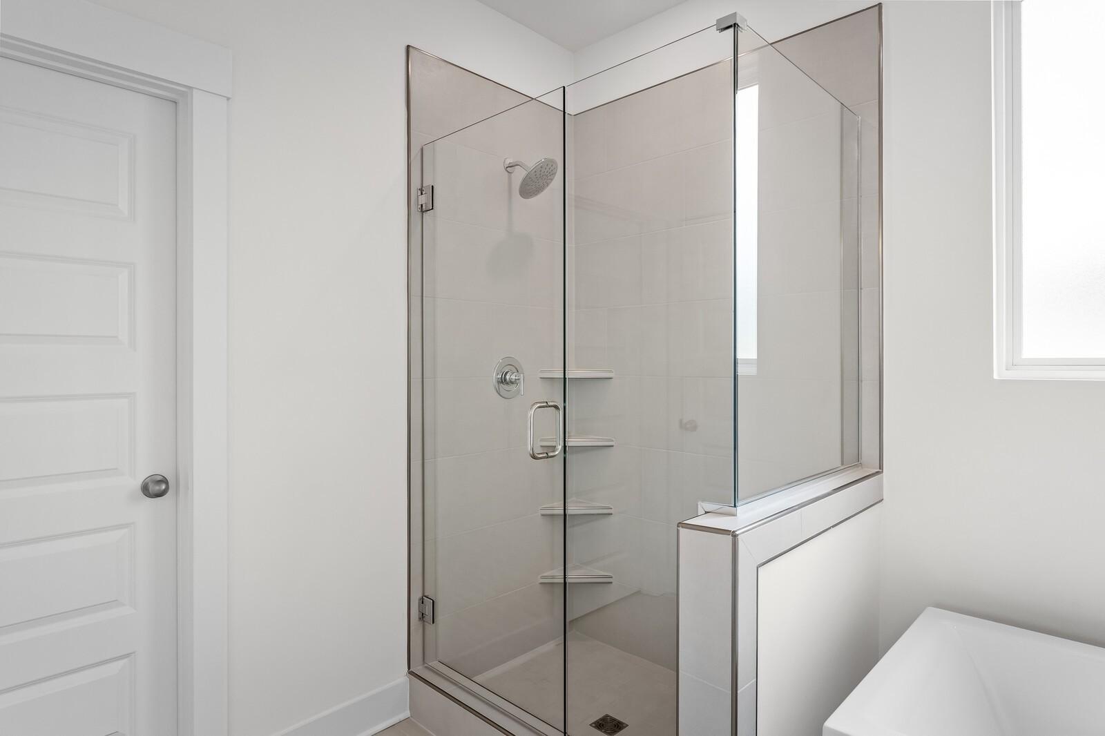 Modern frameless glass walk-in shower with rain showerhead and built-in shelves in master bathroom, Davidson Homes The Ridgeport, Gallatin TN