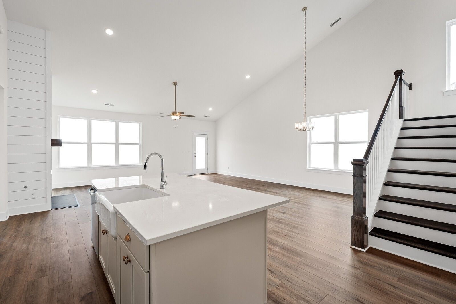 Open-concept kitchen with white quartz island, farmhouse sink, and hardwood floors beside staircase in Ridgeport home, Gallatin, TN