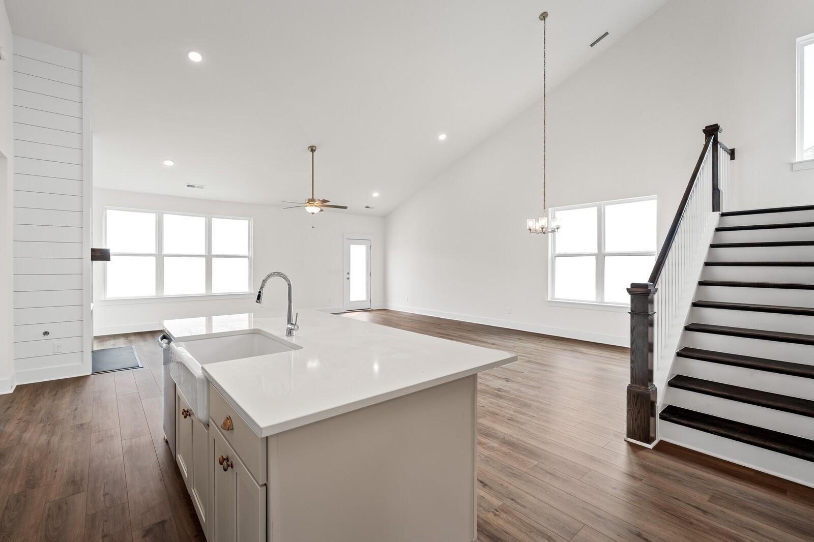 Open-concept kitchen with white quartz island, farmhouse sink, and hardwood floors beside staircase in Ridgeport home, Gallatin, TN