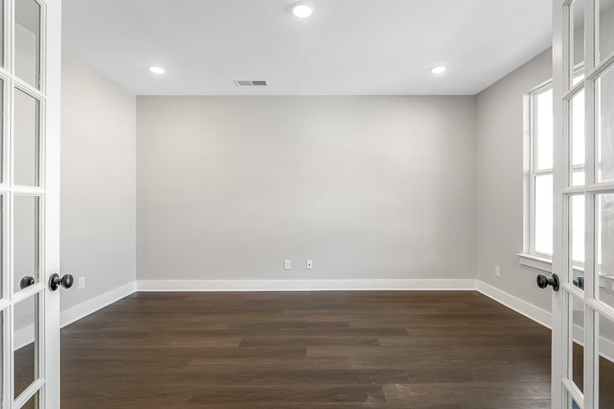 Spacious empty room with light gray walls, dark hardwood floors, French doors, and large windows in Davidson Homes The Henry C, Calista Farms, White House, TN