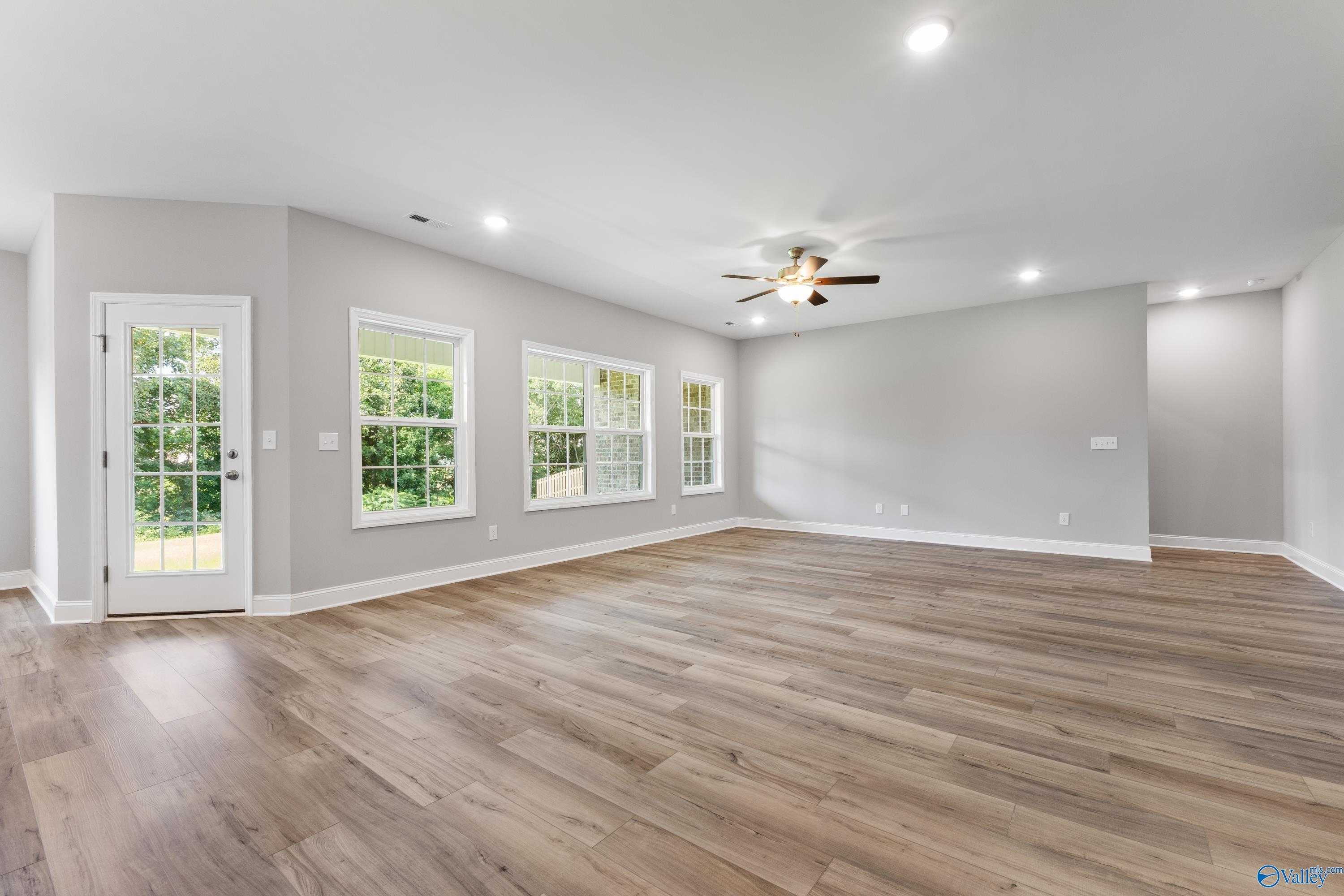 Bright living room with large windows, ceiling fan, recessed lights, and hardwood floors in Davidson Homes The Rockford, Harvest, Alabama