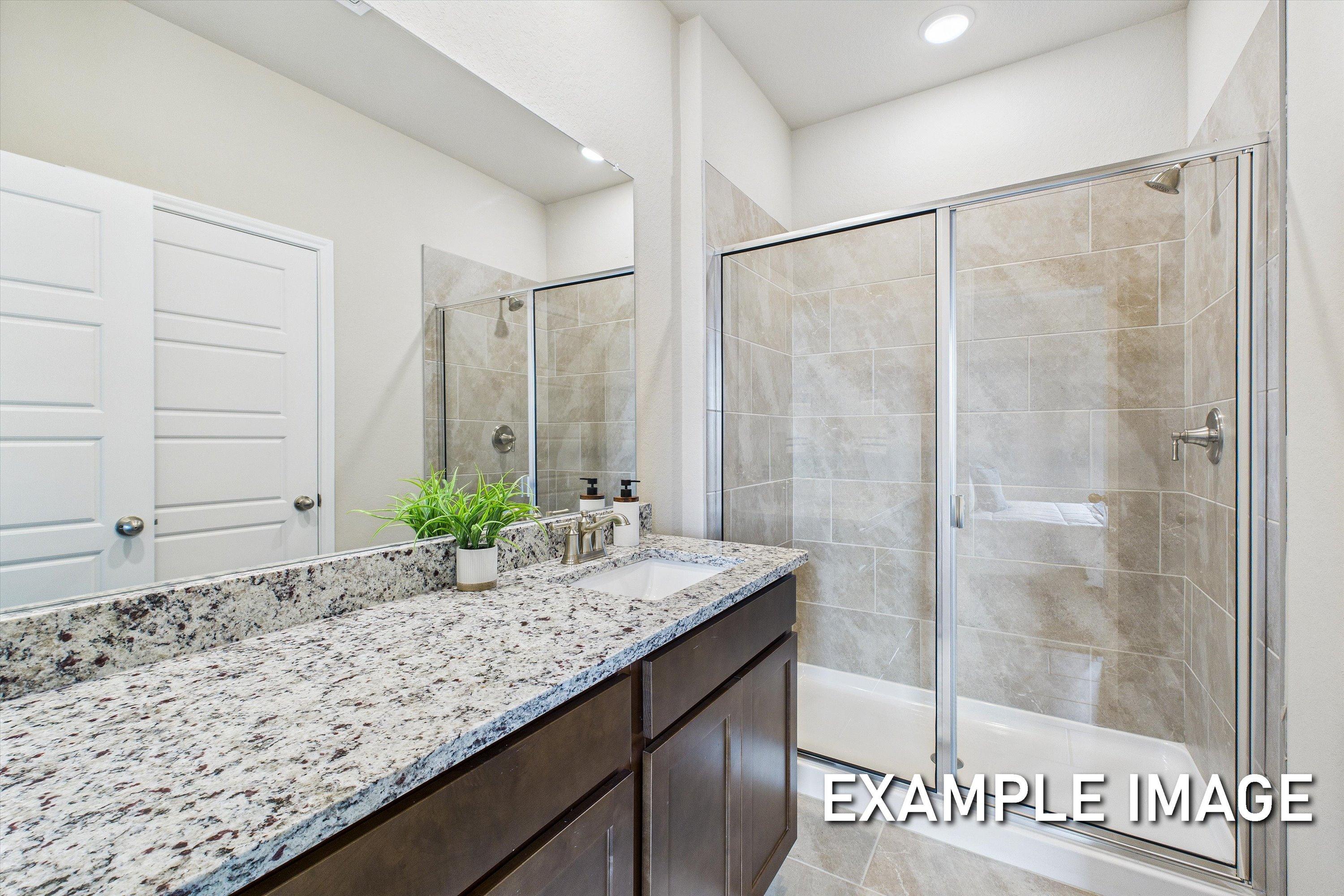 Modern master bathroom in The Comal featuring granite vanity countertops and a tiled walk-in shower.