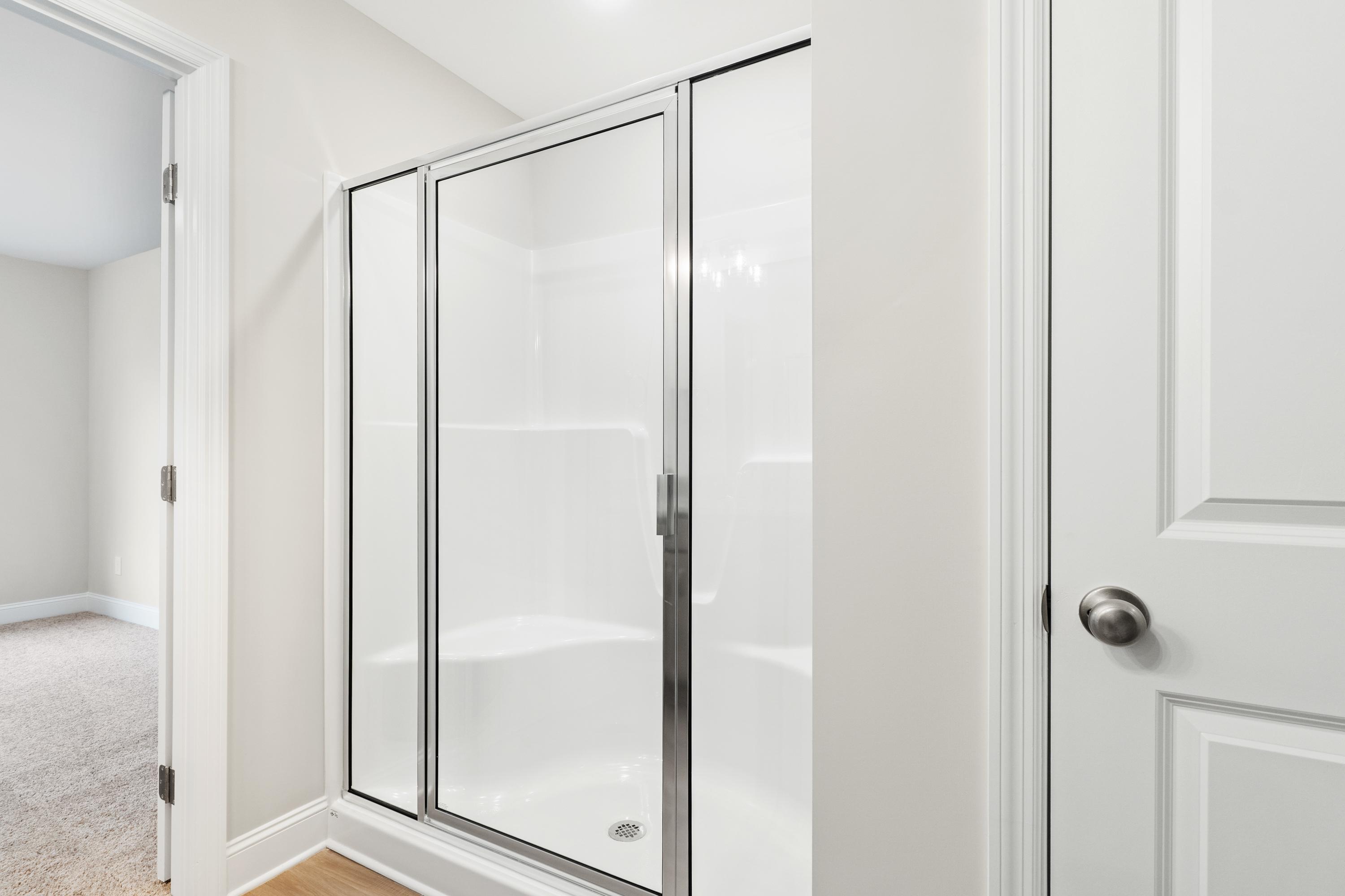 Spacious master bathroom in The Asheville with frameless glass shower, white tile, and adjacent hallway