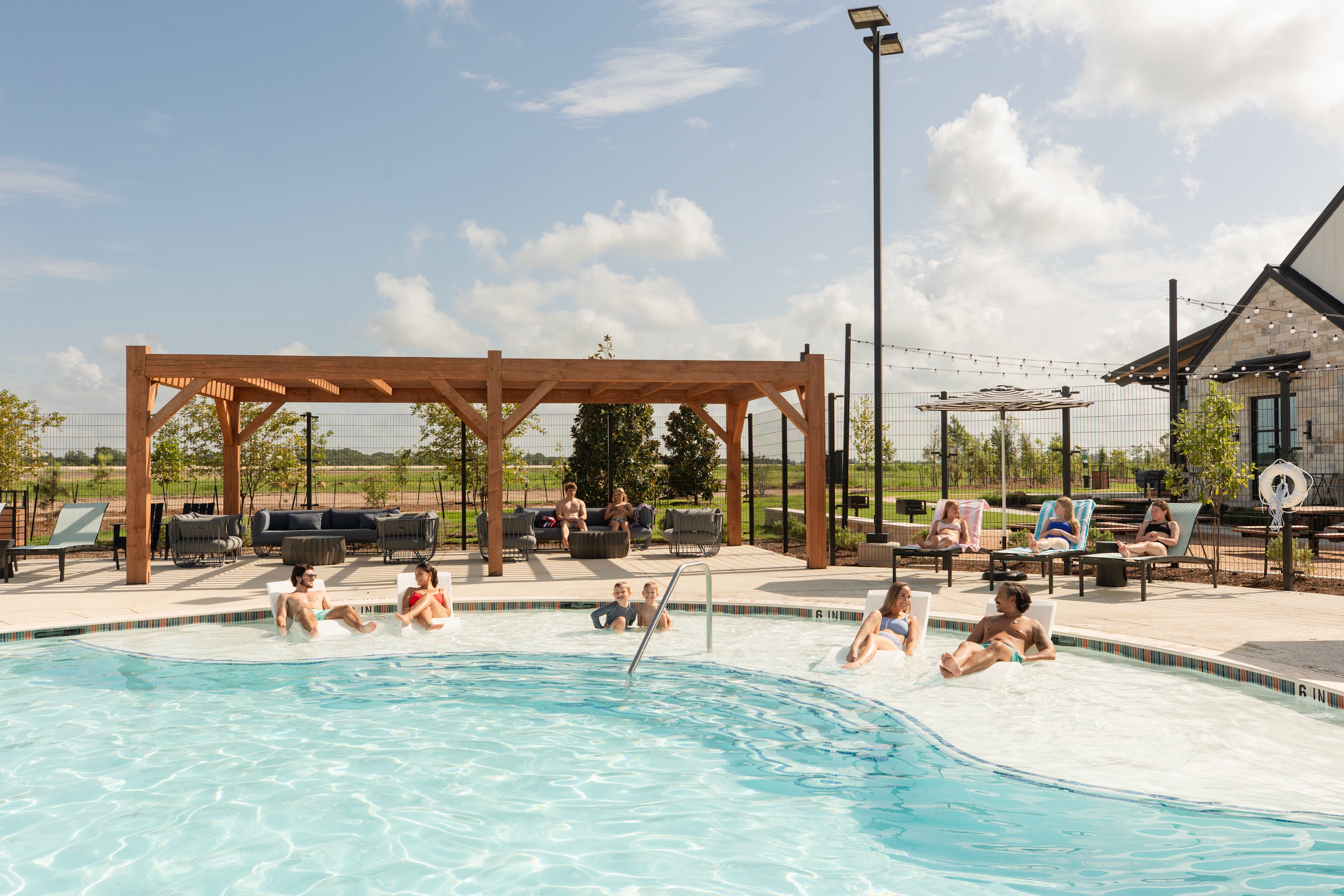 Resort-style pool at Emberly in Beasley Texas with wooden pergola, string lights, lounge seating and residents relaxing