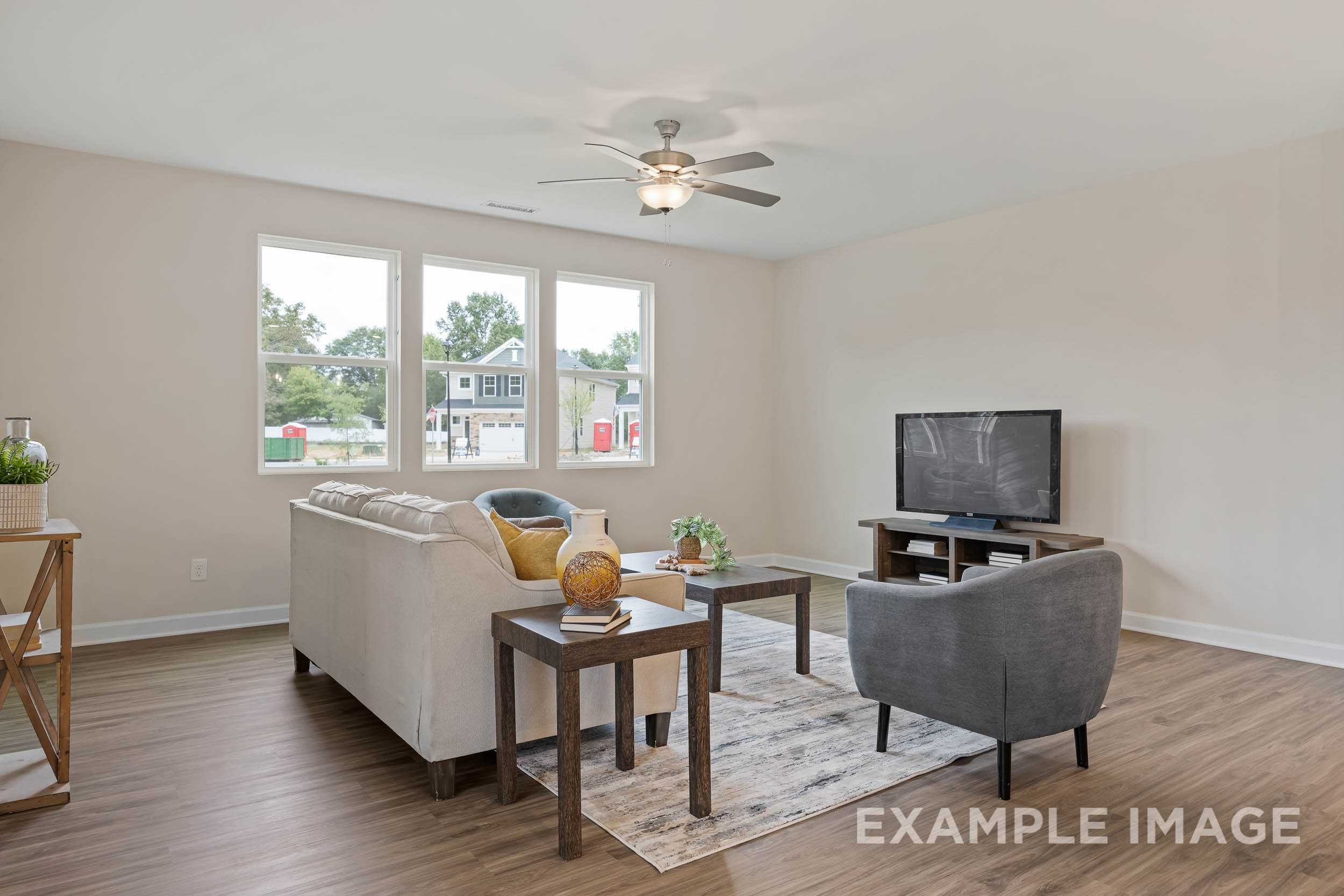 Spacious living room in The Preston B with beige walls, large windows, white sofa, gray armchair, ceiling fan, and hardwood floors