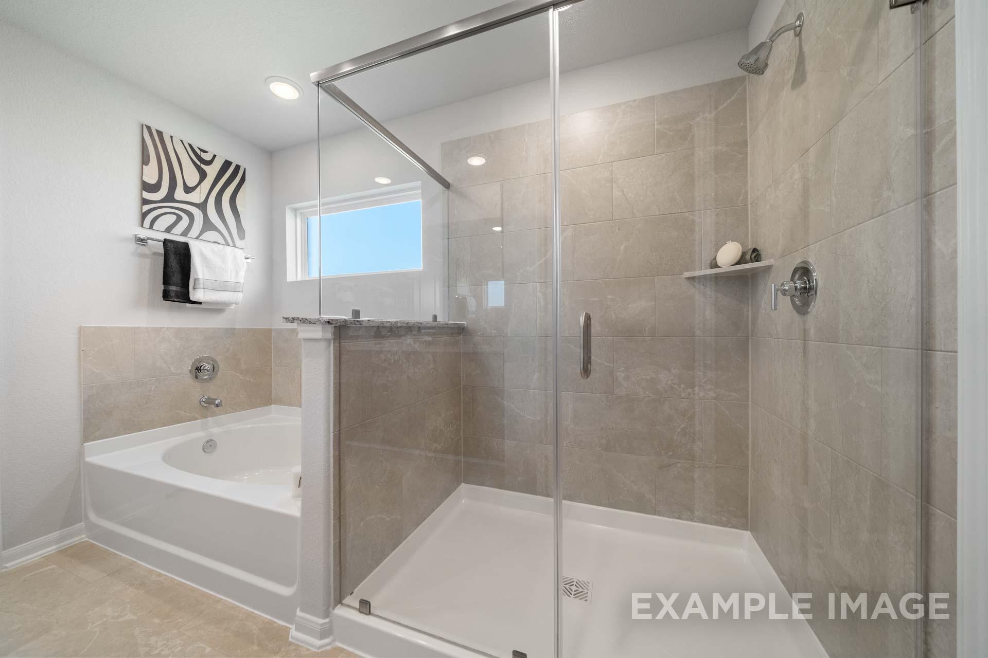 Spacious master bathroom in The Acadia A with frameless glass shower, soaking tub, and neutral tile accents