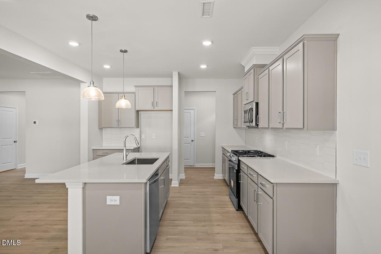 Modern kitchen with gray cabinets, quartz countertops, and island in The Gavin A floor plan, Gregory Village, Lillington, NC.