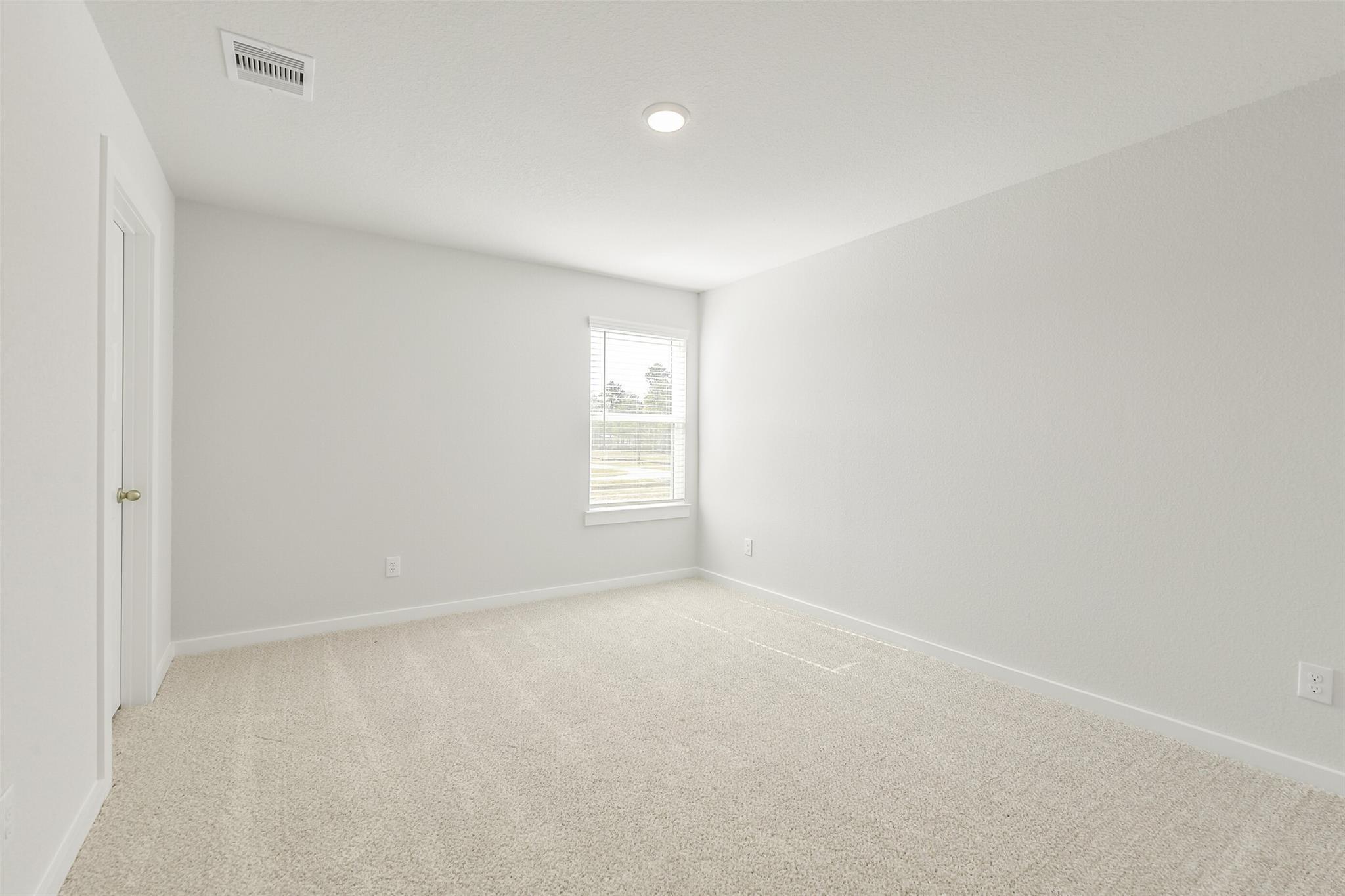 Empty secondary bedroom with light gray walls, beige carpet, large window in Davidson Homes The San Marcos E, Cleveland, Texas