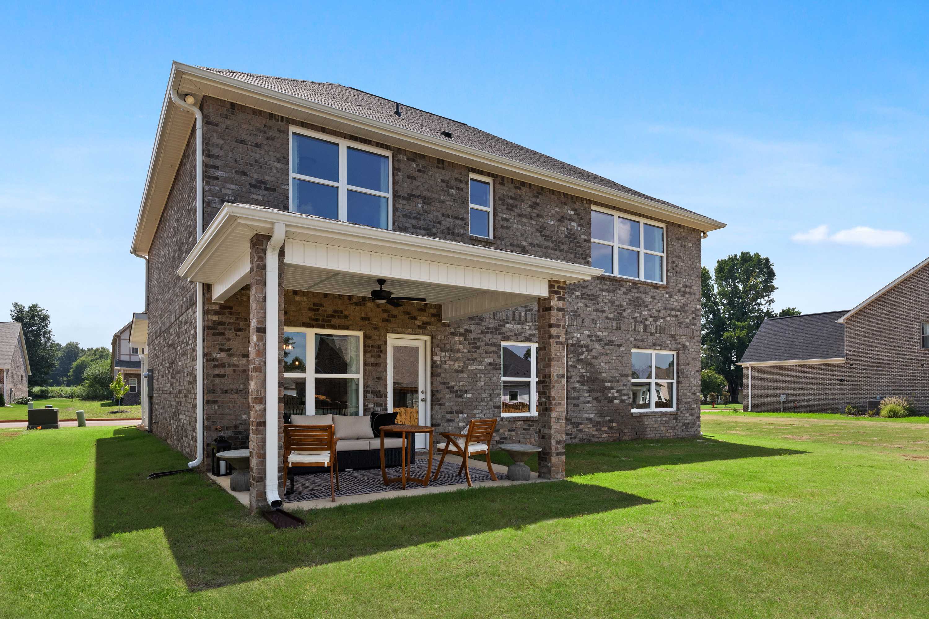 Two-story brick exterior of The Shelby A home with covered porch, ceiling fan, patio furniture, and lush green lawn in Meridianville