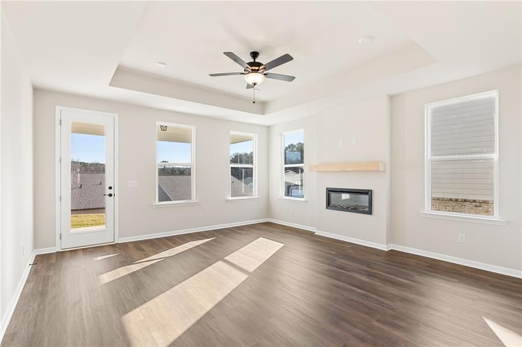 Bright family room with gas fireplace, ceiling fan, hardwood floors, and large windows in The Glenwood A, Loganville, GA