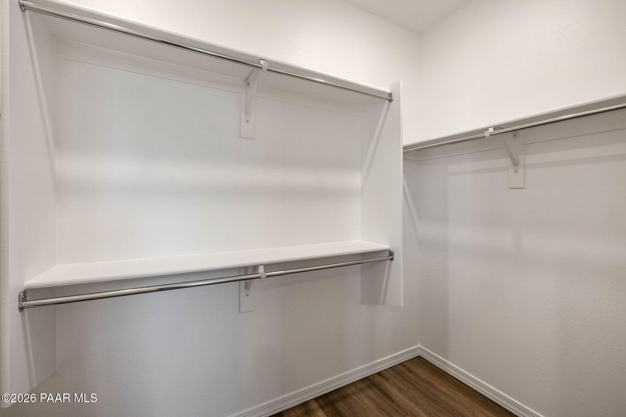 Spacious empty walk-in closet with white shelves and hanging rods on wood floors in Davidson Homes The Frontier A, Prescott Valley