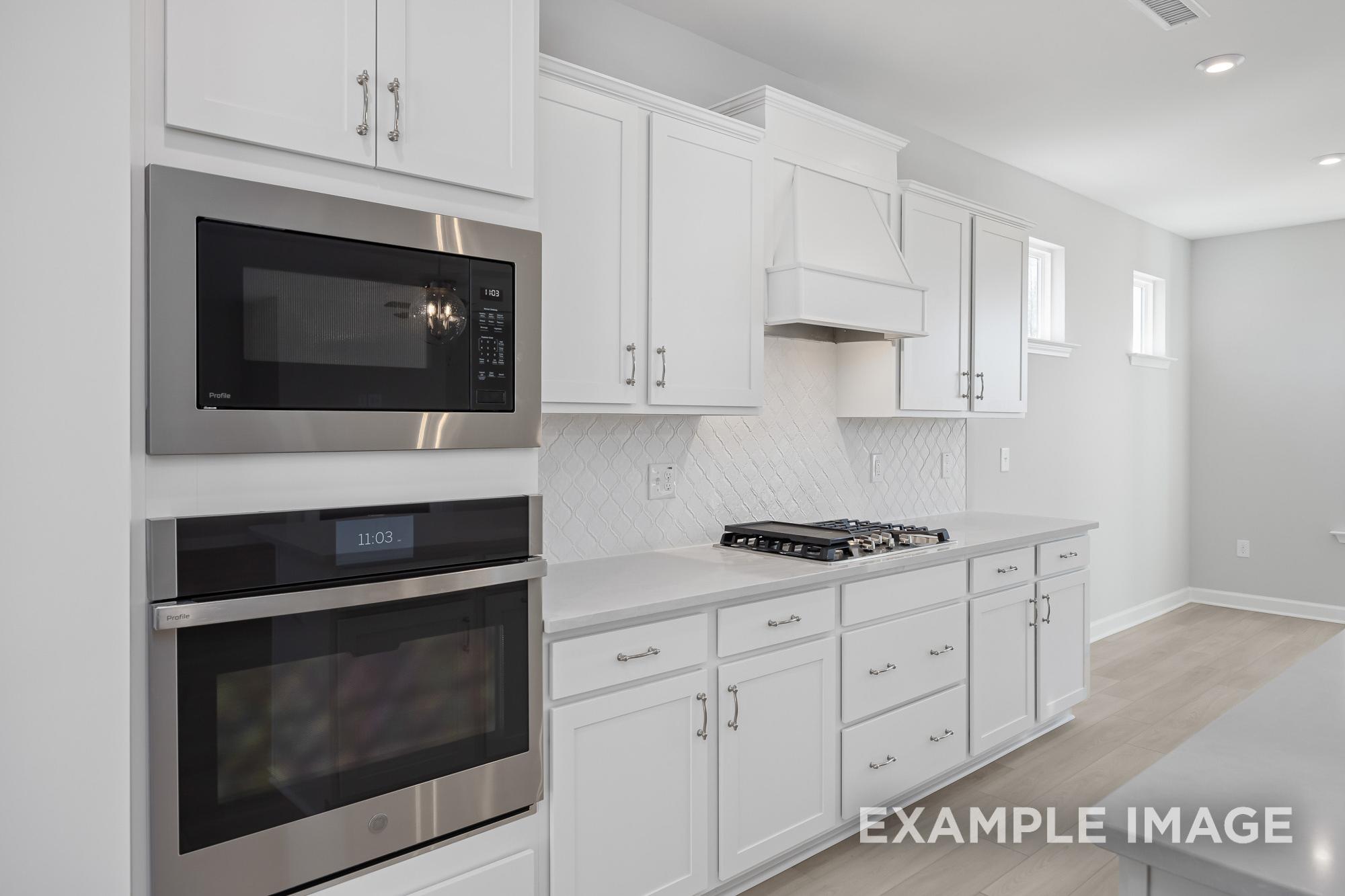 Spacious kitchen in The Cypress C II with white shaker cabinets, stainless steel built-in oven and microwave, gas cooktop, quartz counters